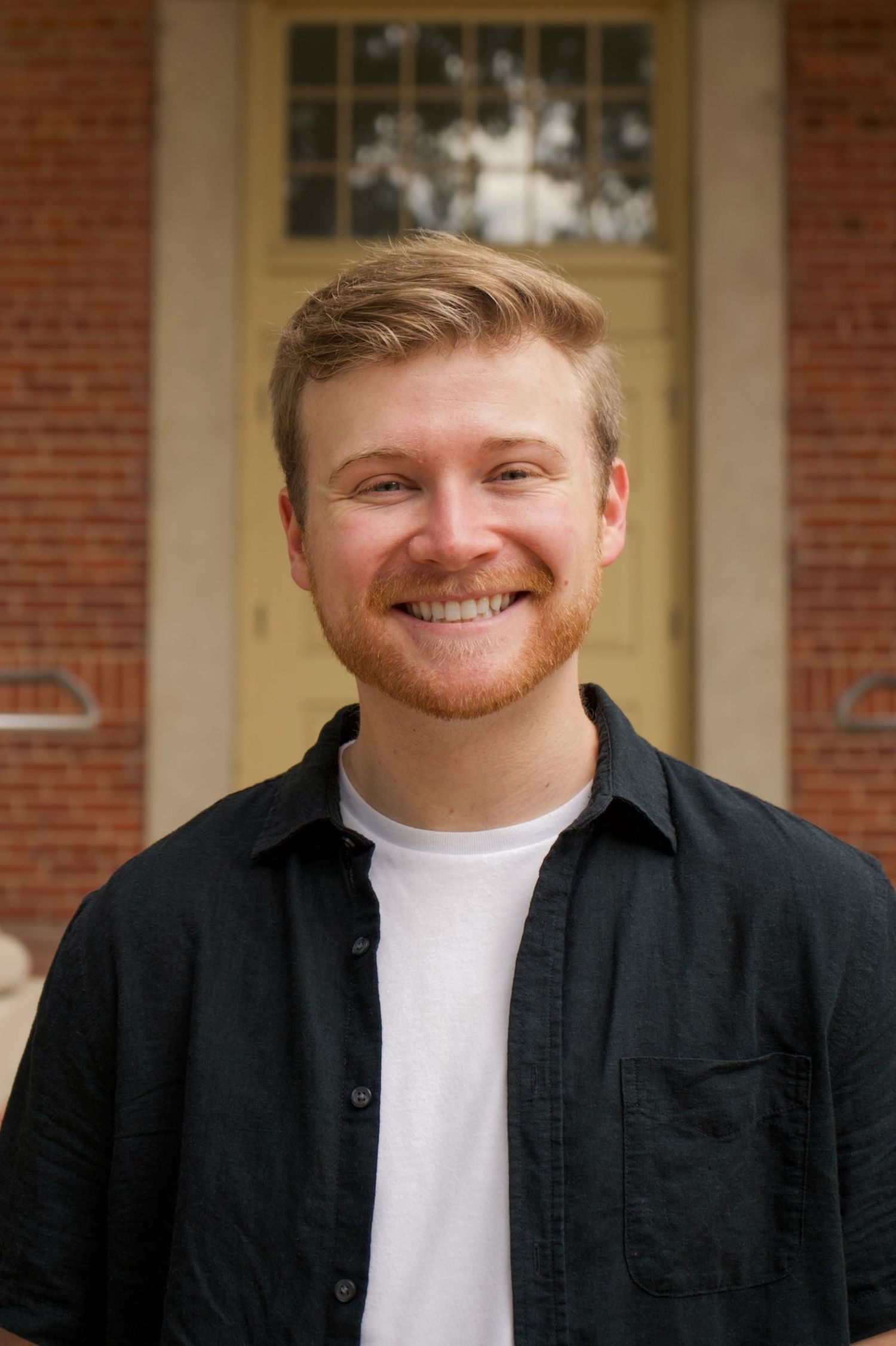 Headshot of smiling young man with red beard.
