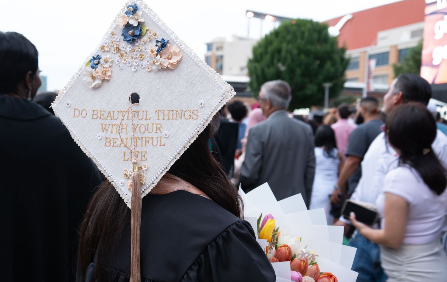 Decorated graduation mortarboard with floral design and inspirational quote at outdoor ceremony.