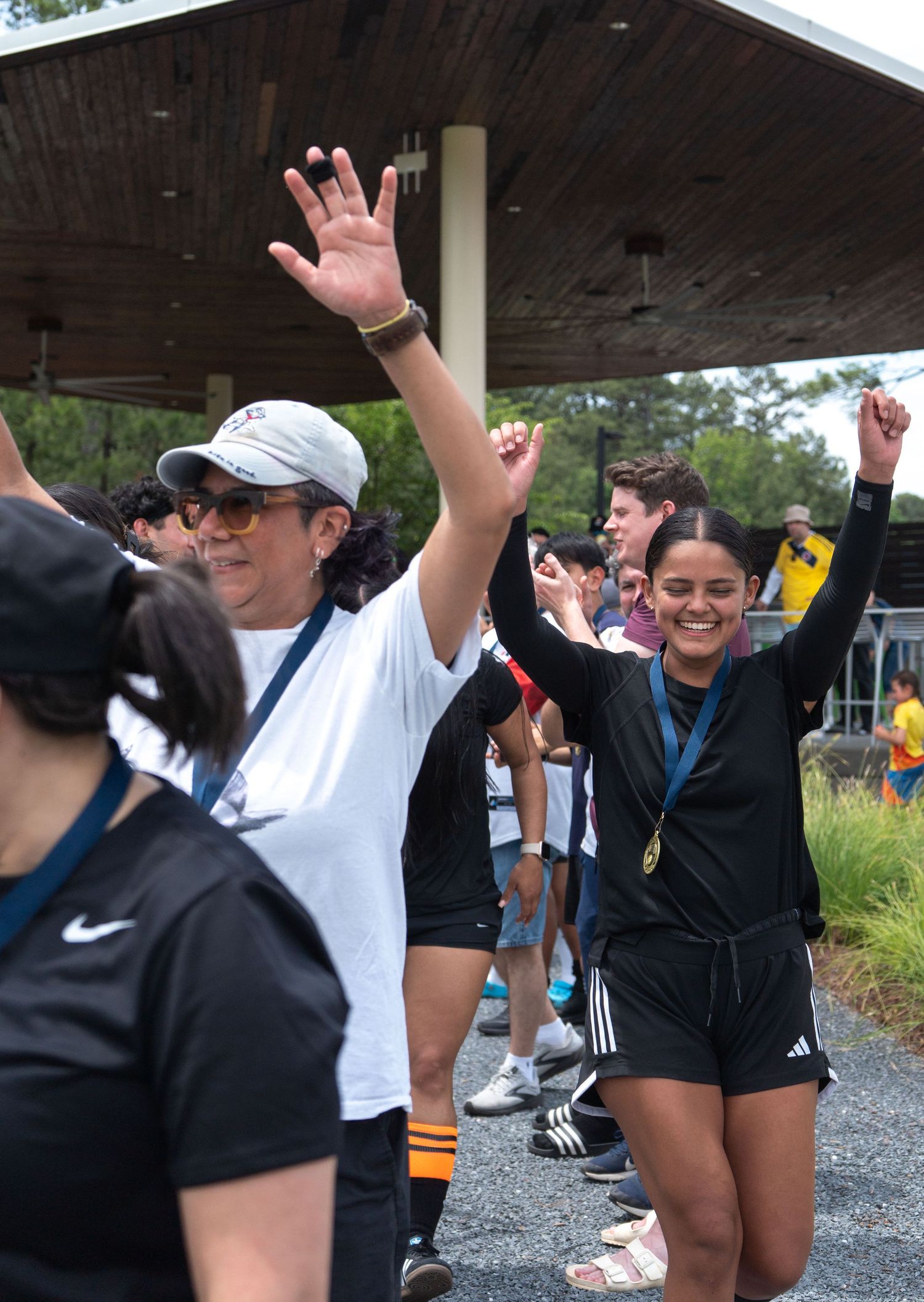 Excited woman with medal raises hands in celebration at outdoor sports event with crowd.