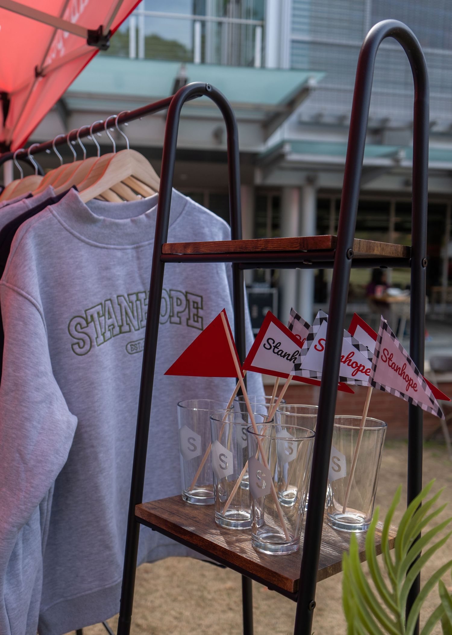 Stanhope branded sweatshirt, glasses, and mini flags displayed on a ladder shelf at an outdoor event.