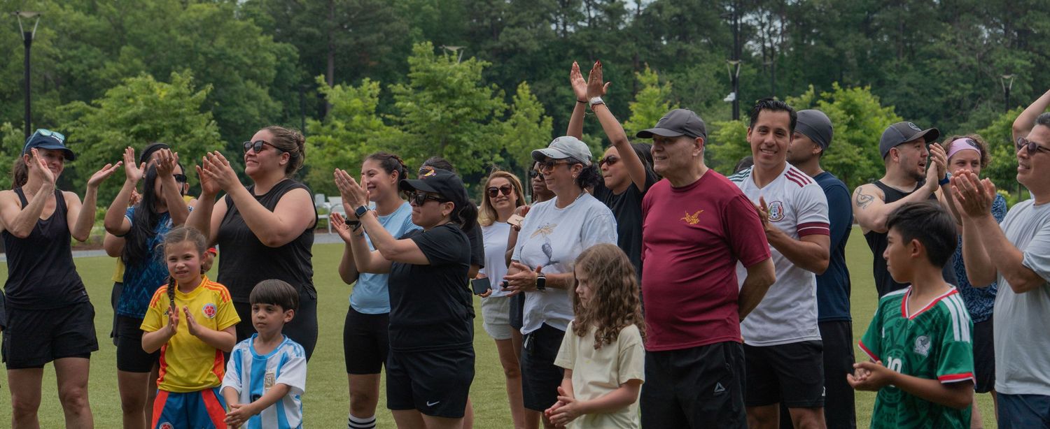 Crowd of people clapping and cheering outdoors on a green field at a community sports event.