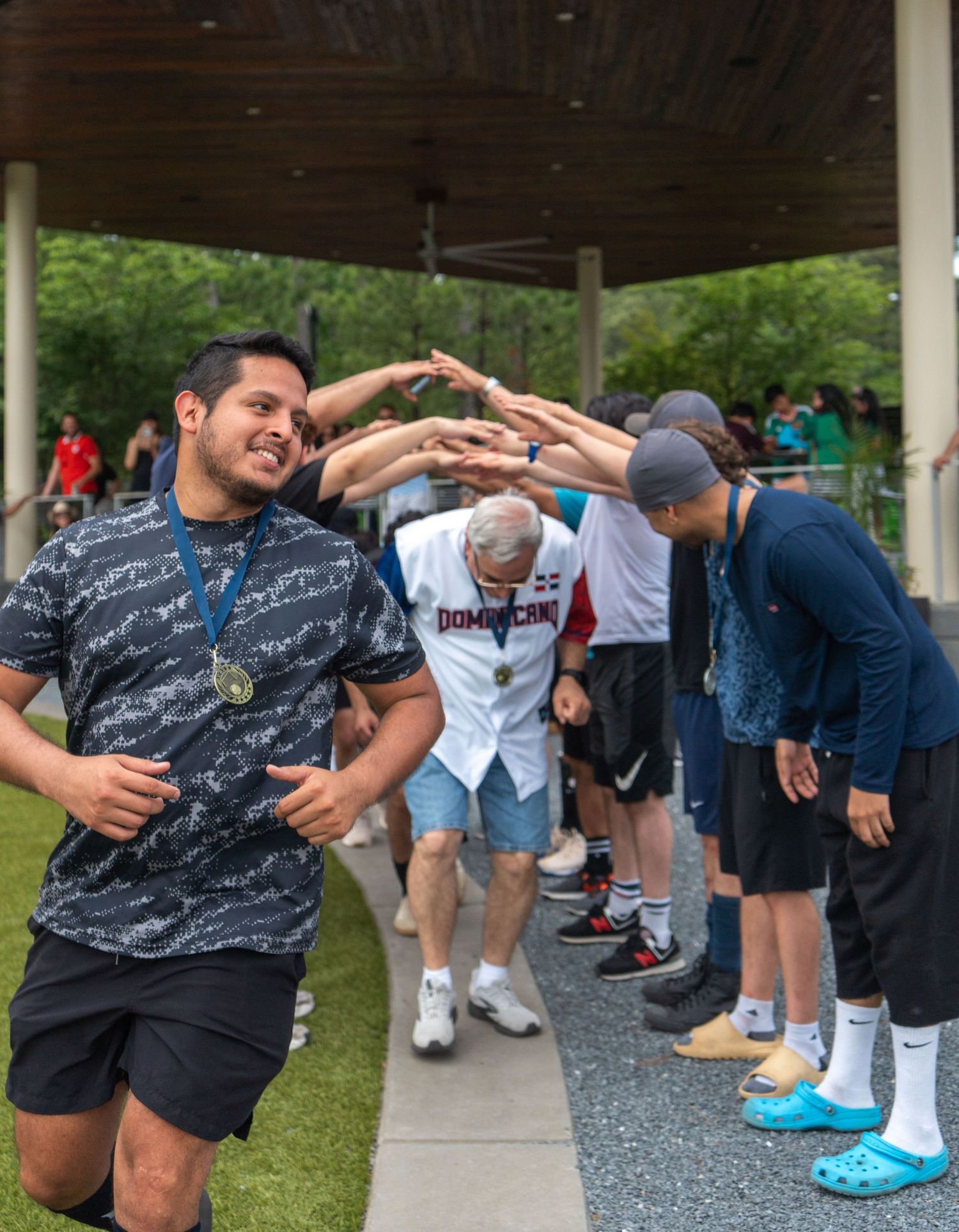 Smiling man with medal runs through congratulatory tunnel of people at outdoor sports event.