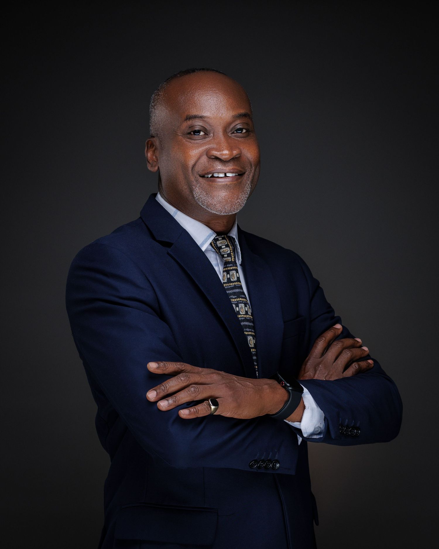 Professional man in navy blue suit with arms crossed smiling confidently in corporate portrait.