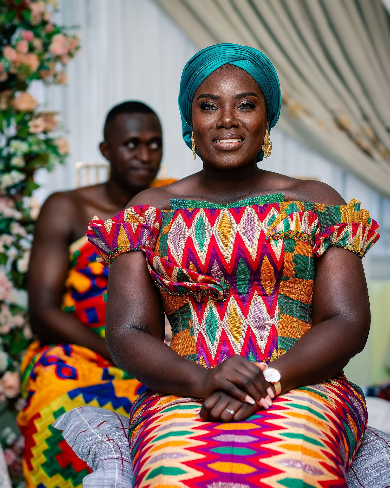 A woman in colorful Kente fabric smiles at an African traditional wedding ceremony.