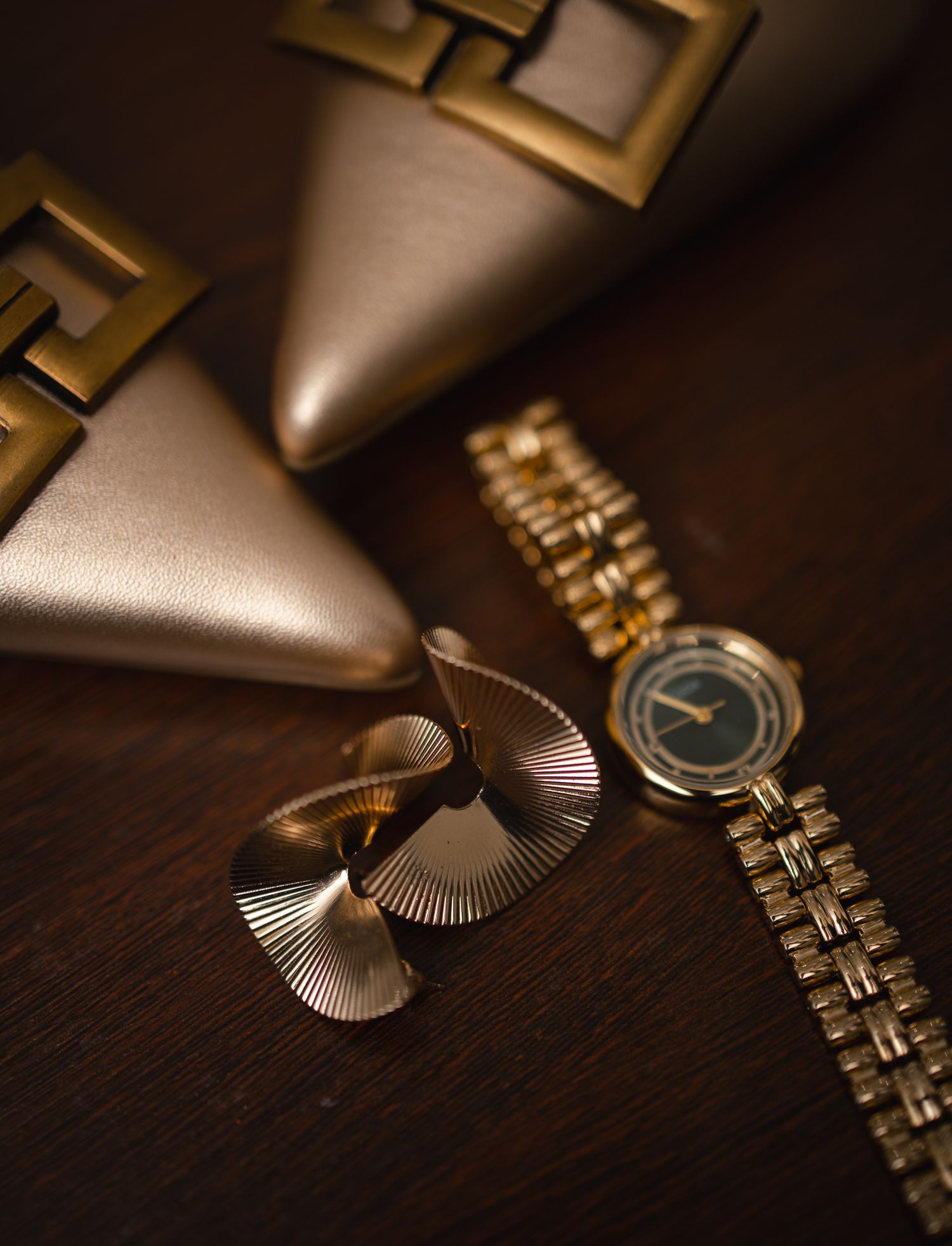 Gold wedding accessories including a watch, fan earrings, and heeled shoes arranged on a wooden surface.