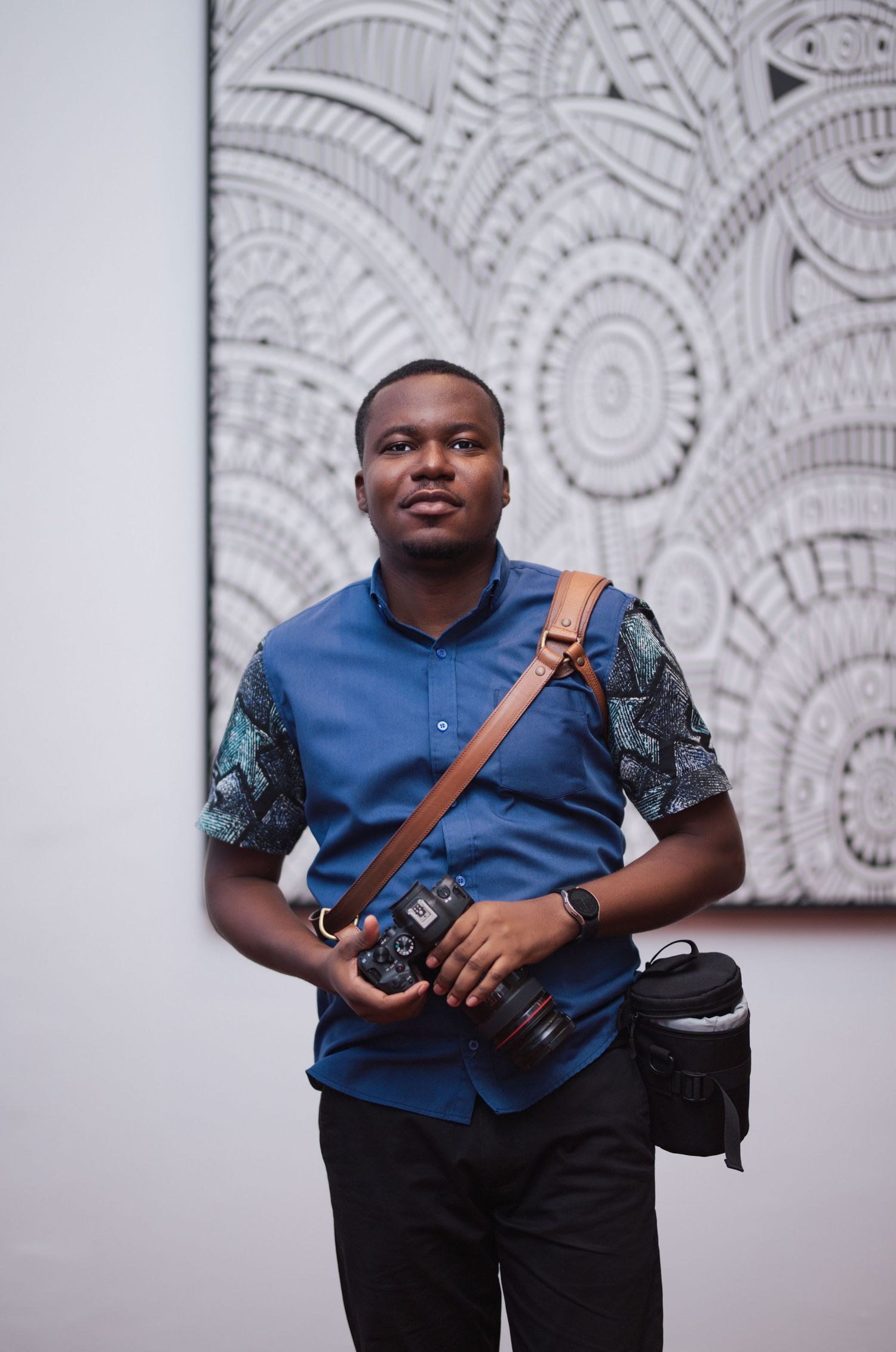 Photographer in blue shirt holds camera while standing before abstract black and white artwork.