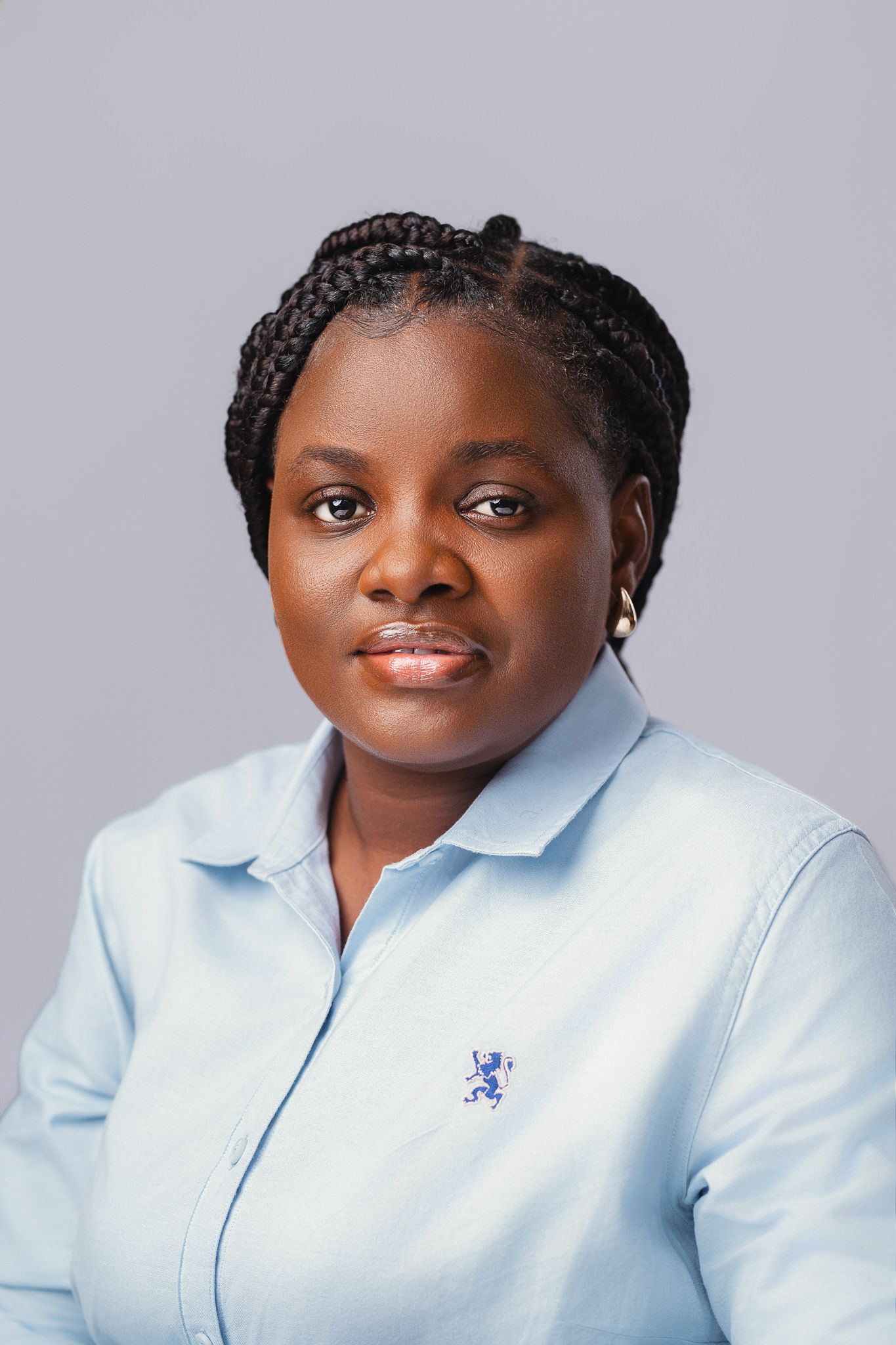 Black woman with box braids in blue collared shirt, posing for professional headshot on gray background.