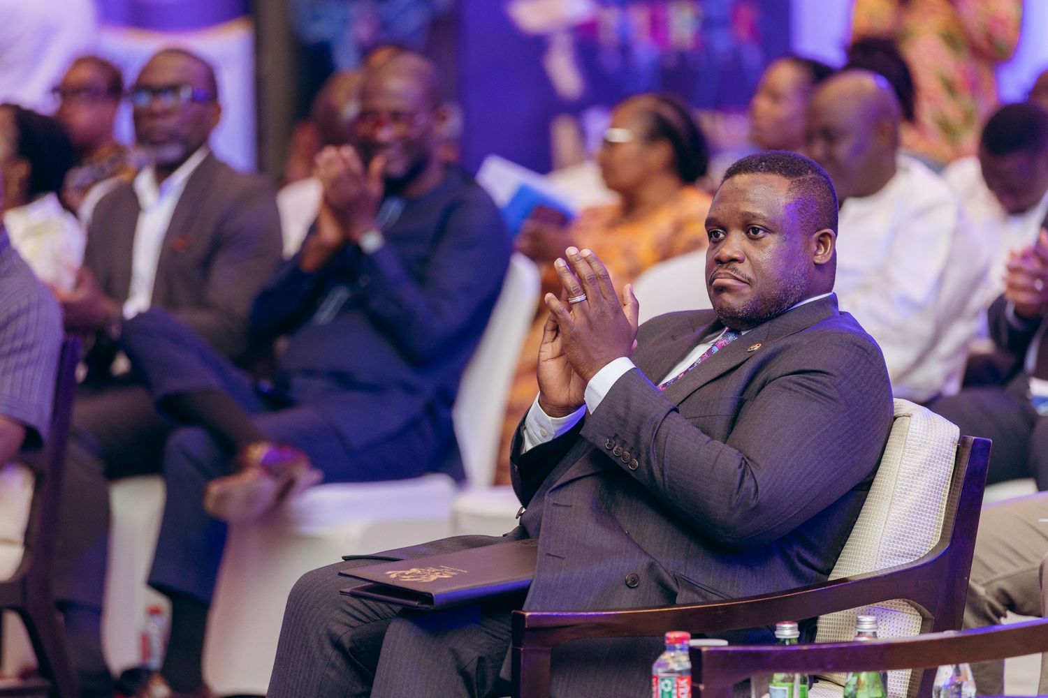 Well-dressed man applauding at formal business conference seated in elegant venue.
