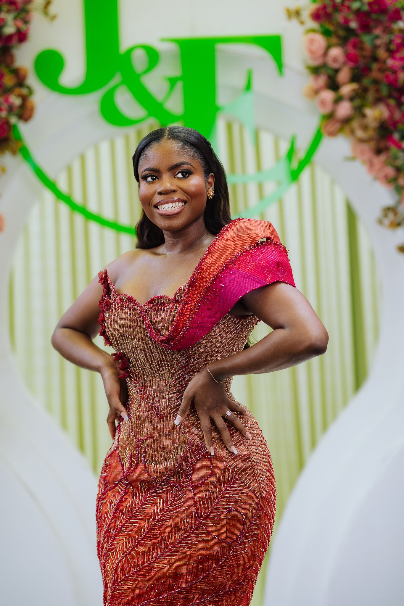 A woman in a beaded red and pink off-shoulder gown poses at a J&E wedding celebration.