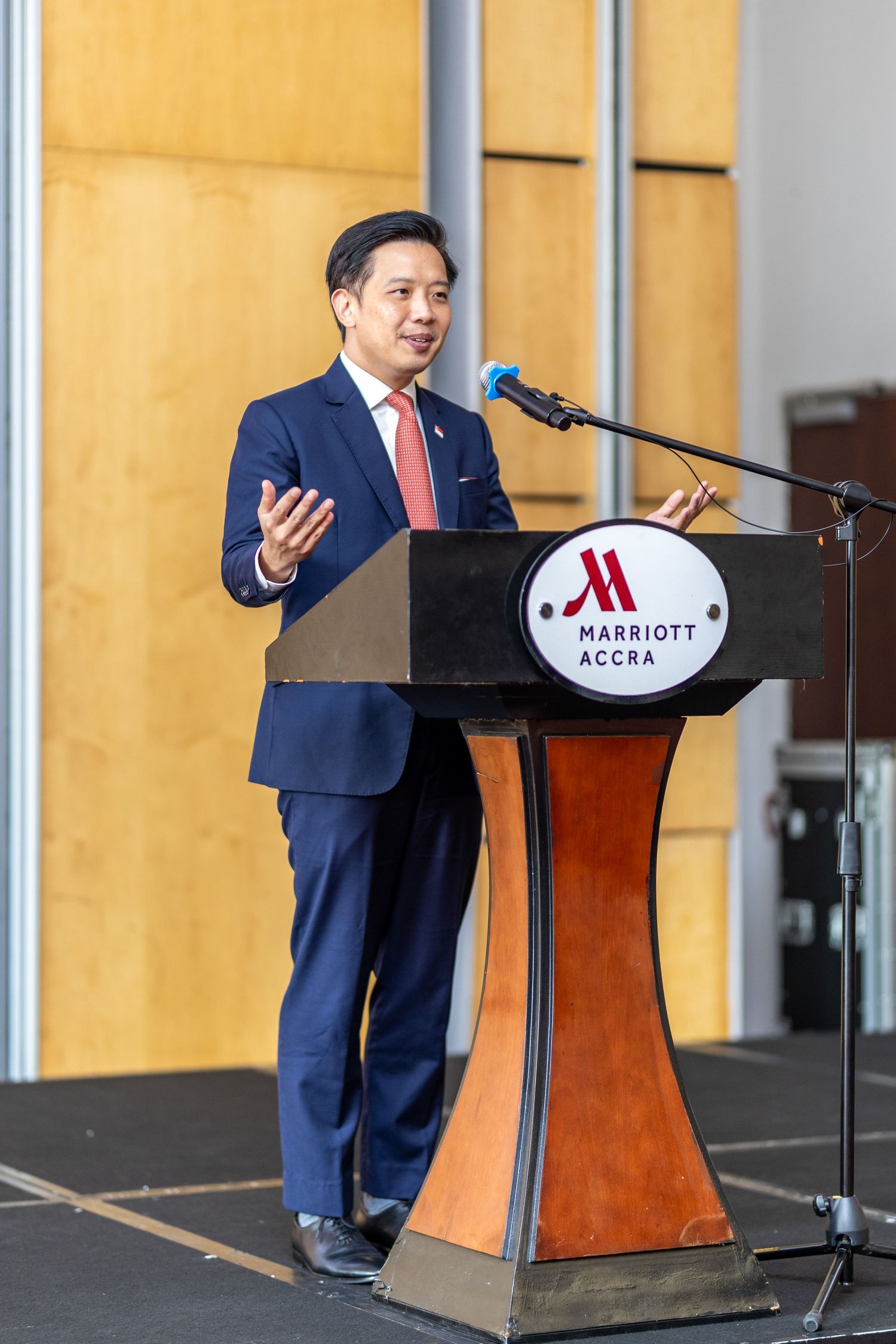 Business speaker gesturing at Marriott Accra lectern during corporate presentation event.