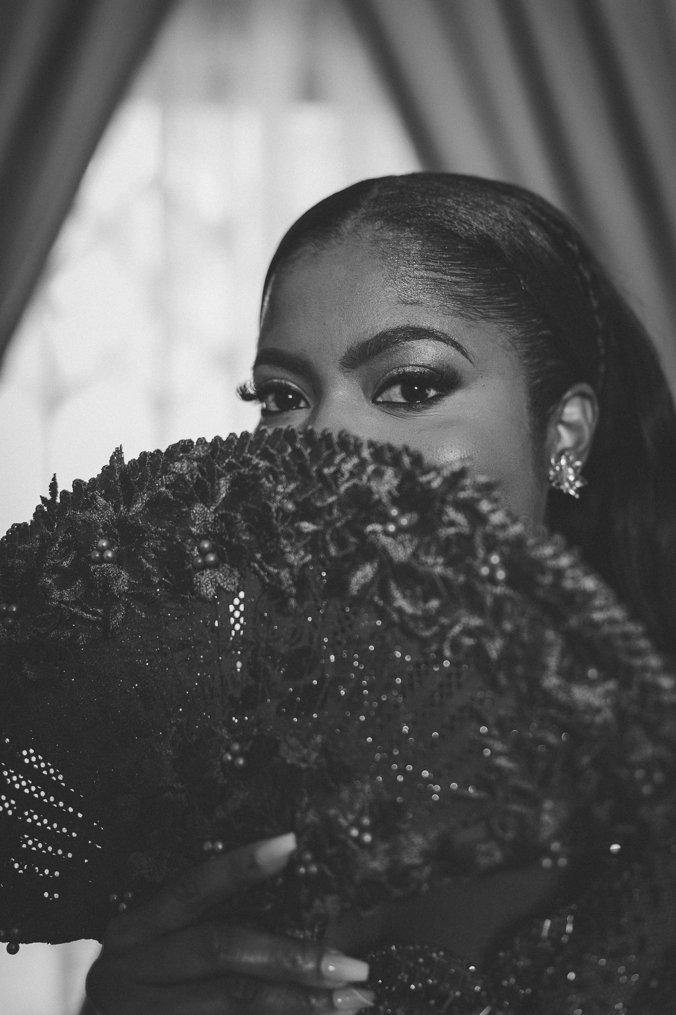 Black and white portrait of bride with dramatic eye makeup partially hidden behind ornate dark fan.