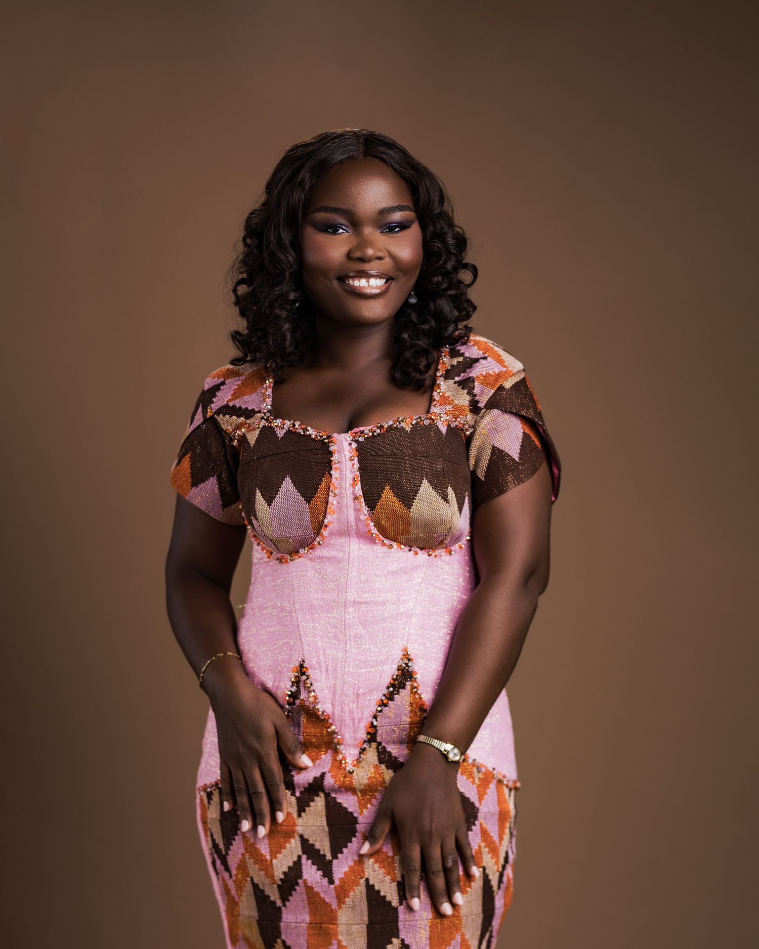 Young woman in traditional pink kente dress smiling in professional studio portrait.