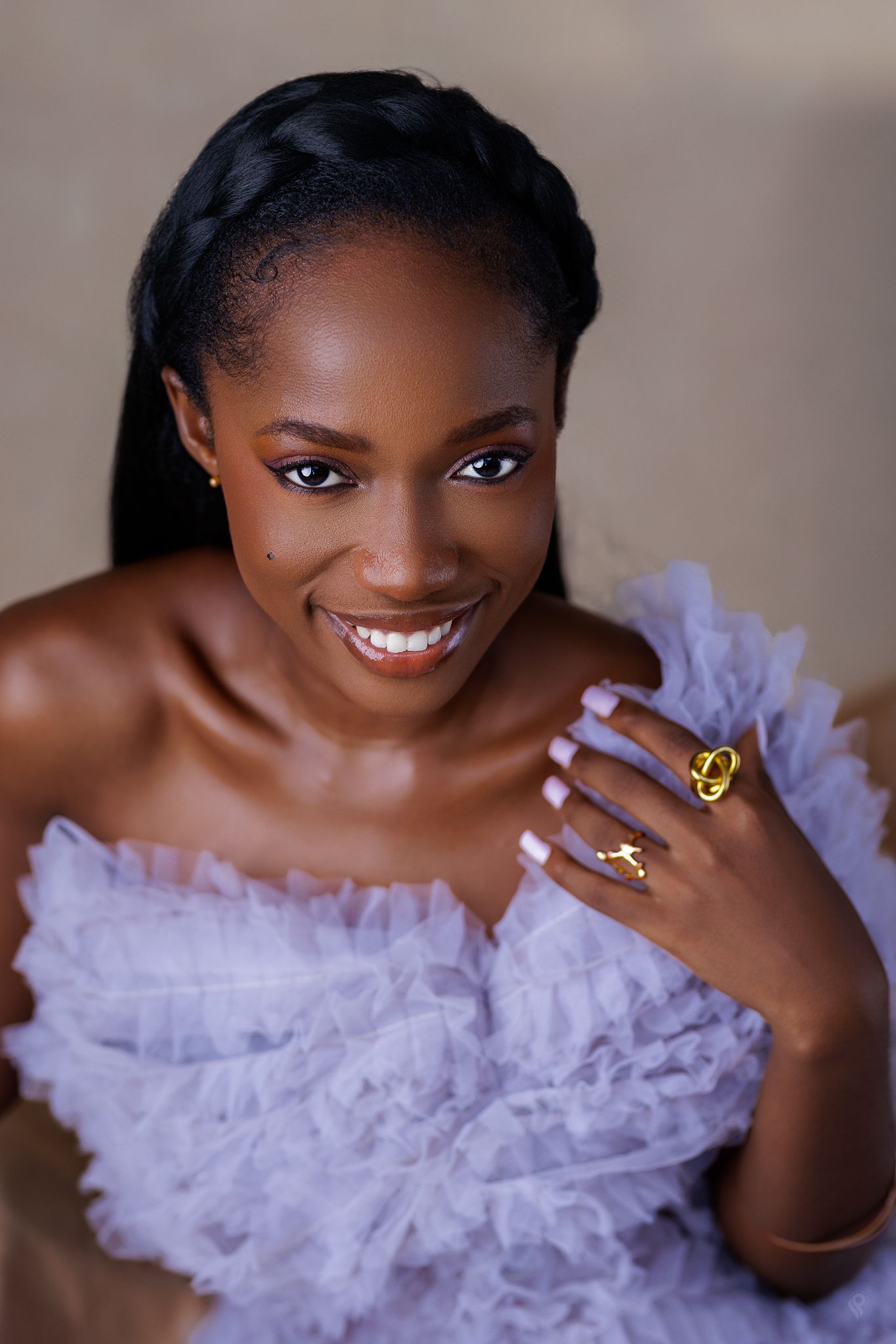 Close-up portrait of a smiling woman in lavender ruffled dress wearing a gold cross ring.