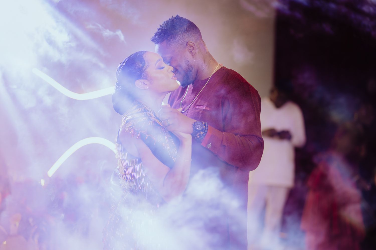 A couple shares a romantic kiss surrounded by dramatic purple smoke and stage lighting.