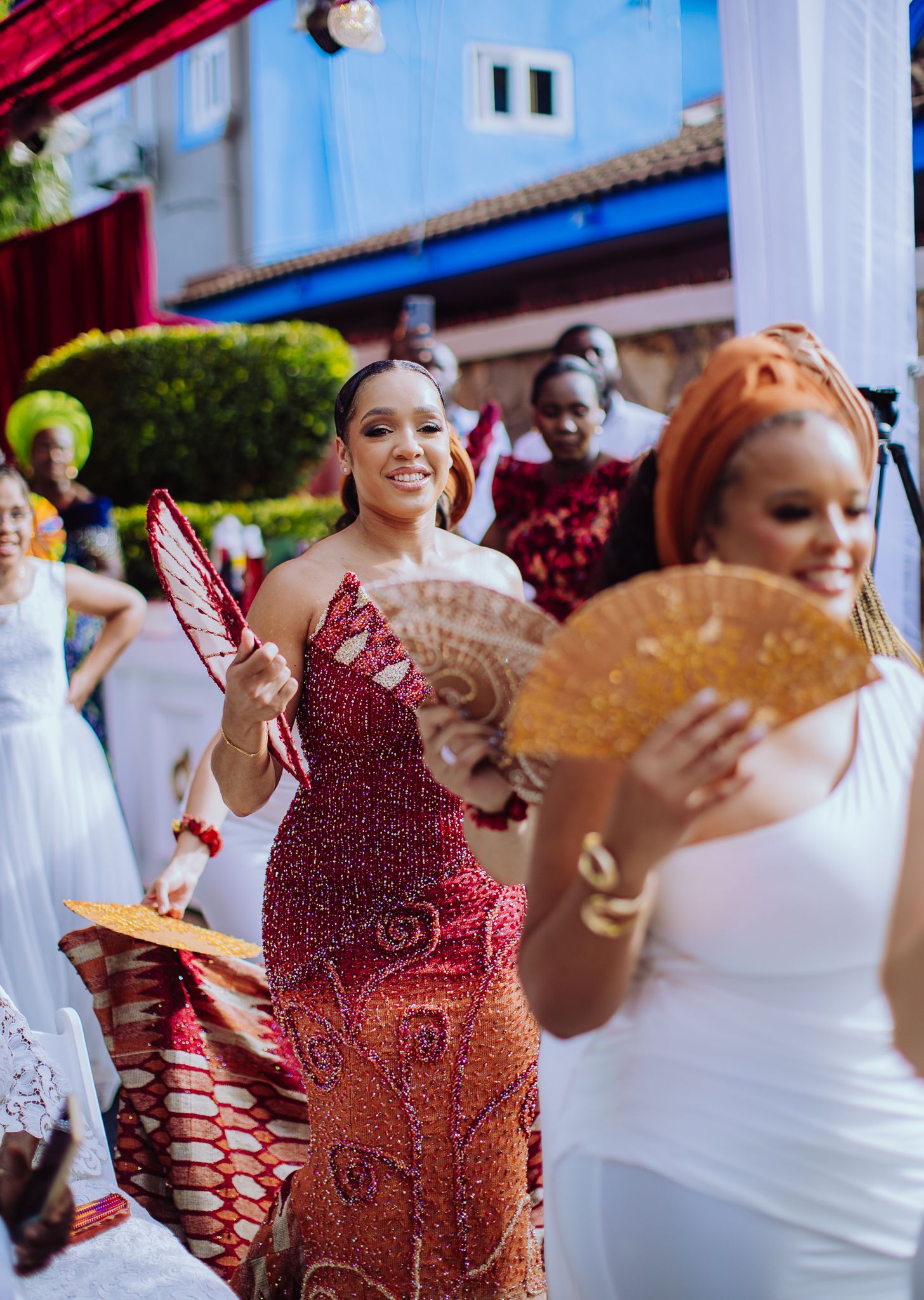 Women in vibrant traditional African attire dancing with decorative fans at a colorful outdoor cultural celebration.
