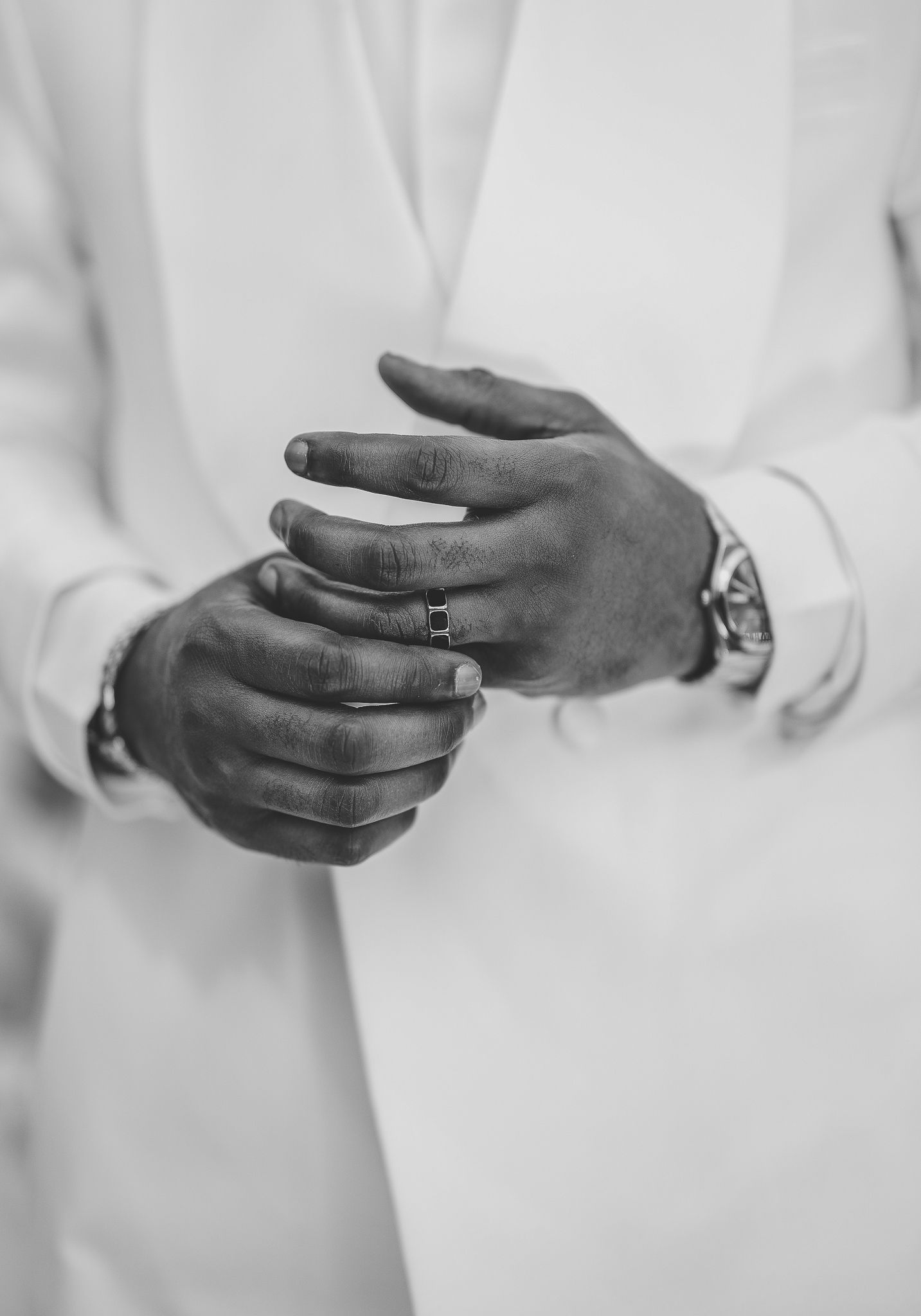 Close-up of a groom adjusting his wedding ring, wearing a white suit and watch.