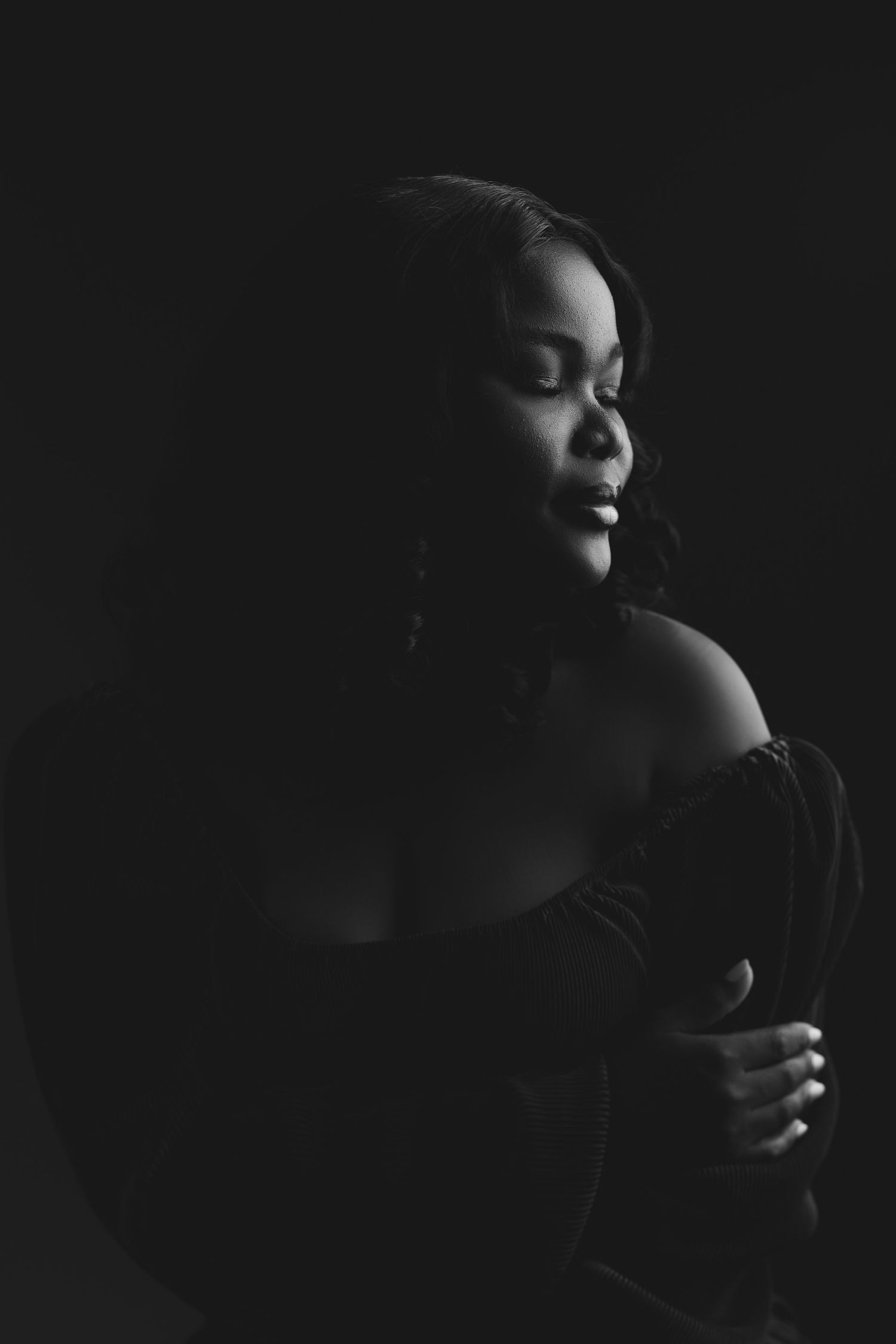 Artistic black and white portrait of a Black woman with closed eyes in dramatic low-key lighting.