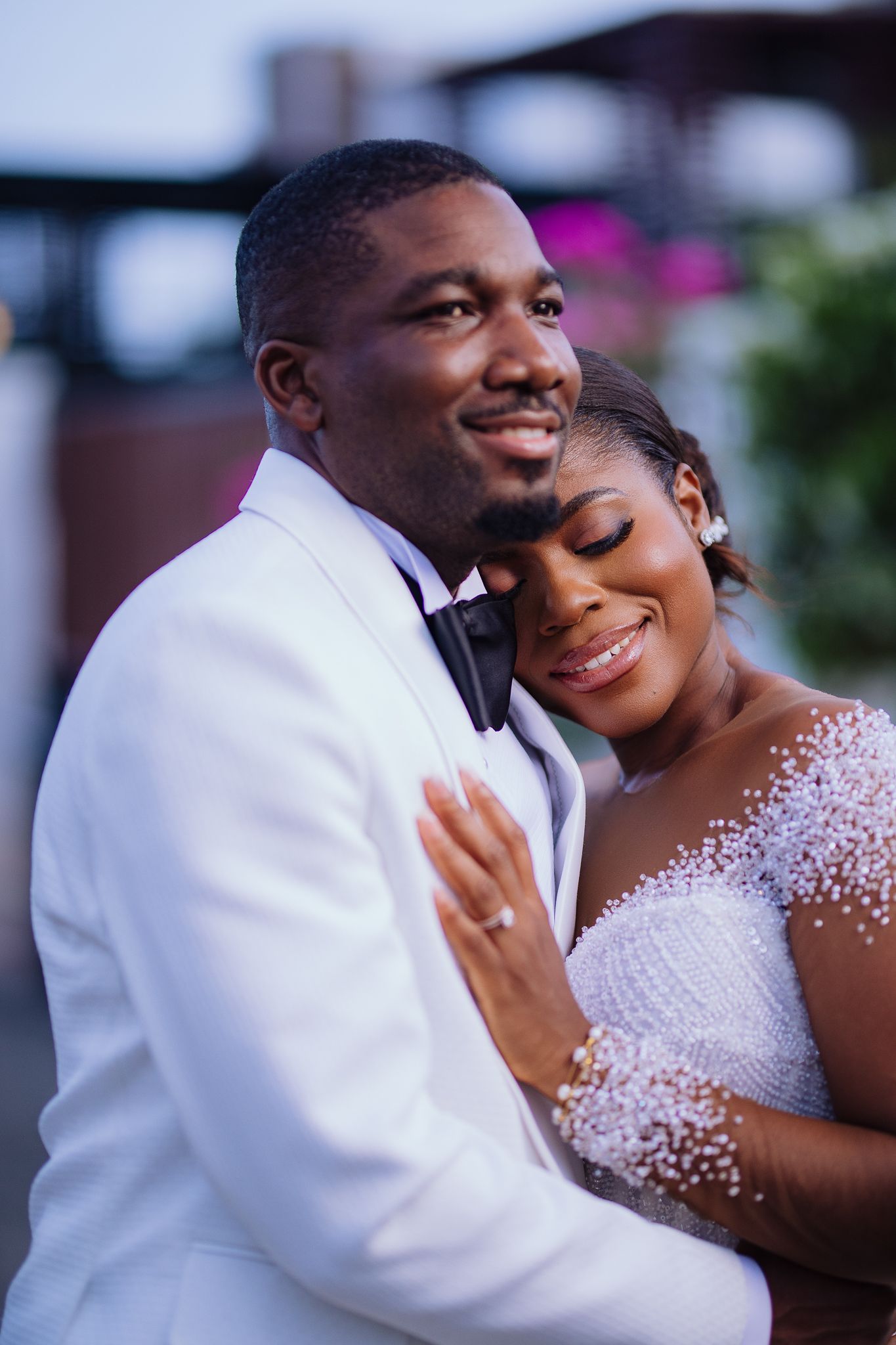 Elegant couple embracing at dusk, groom in white tuxedo and bride in beaded wedding gown.