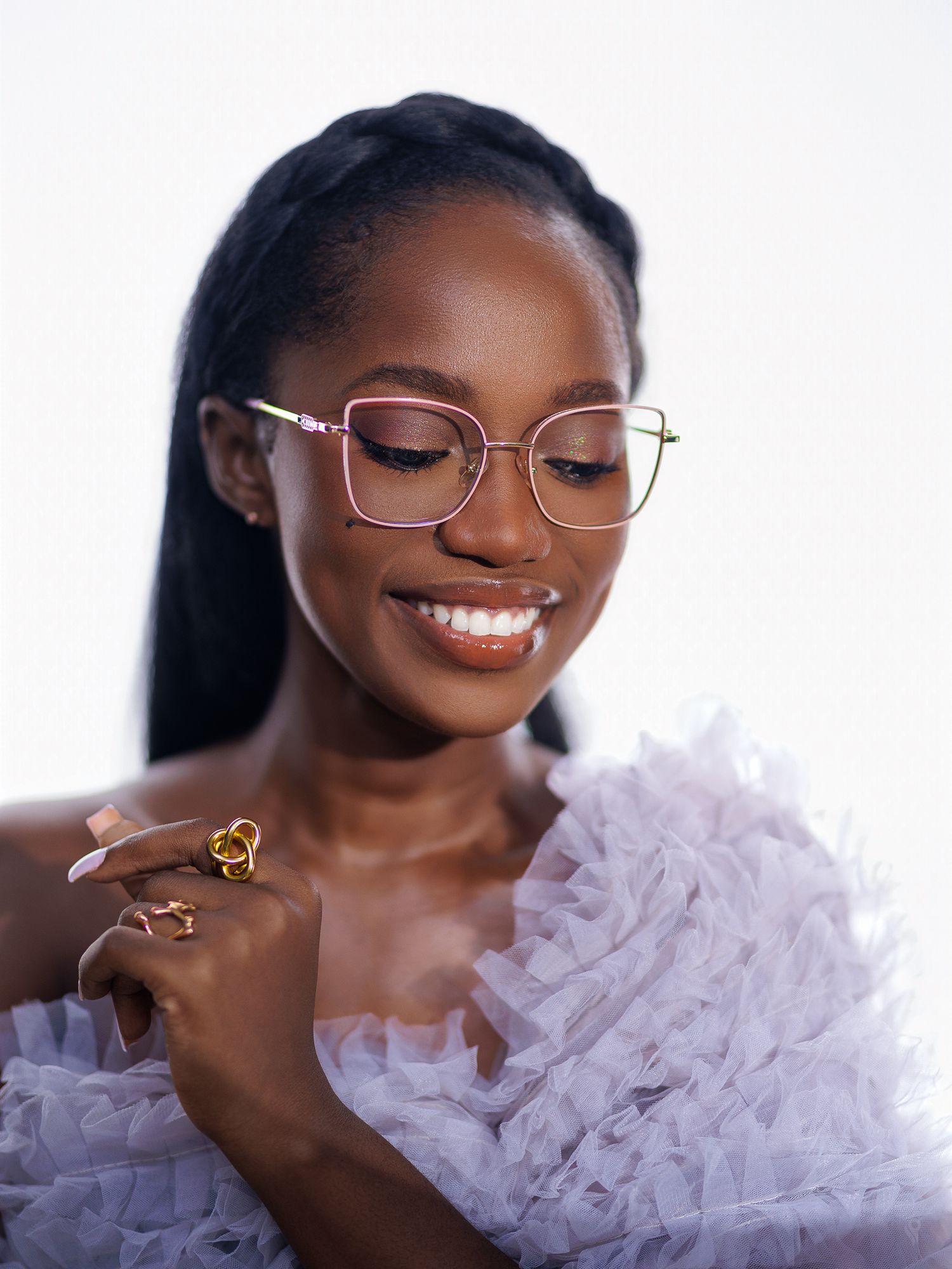 Elegant Black woman wearing square glasses and lavender ruffled dress, smiling downward.
