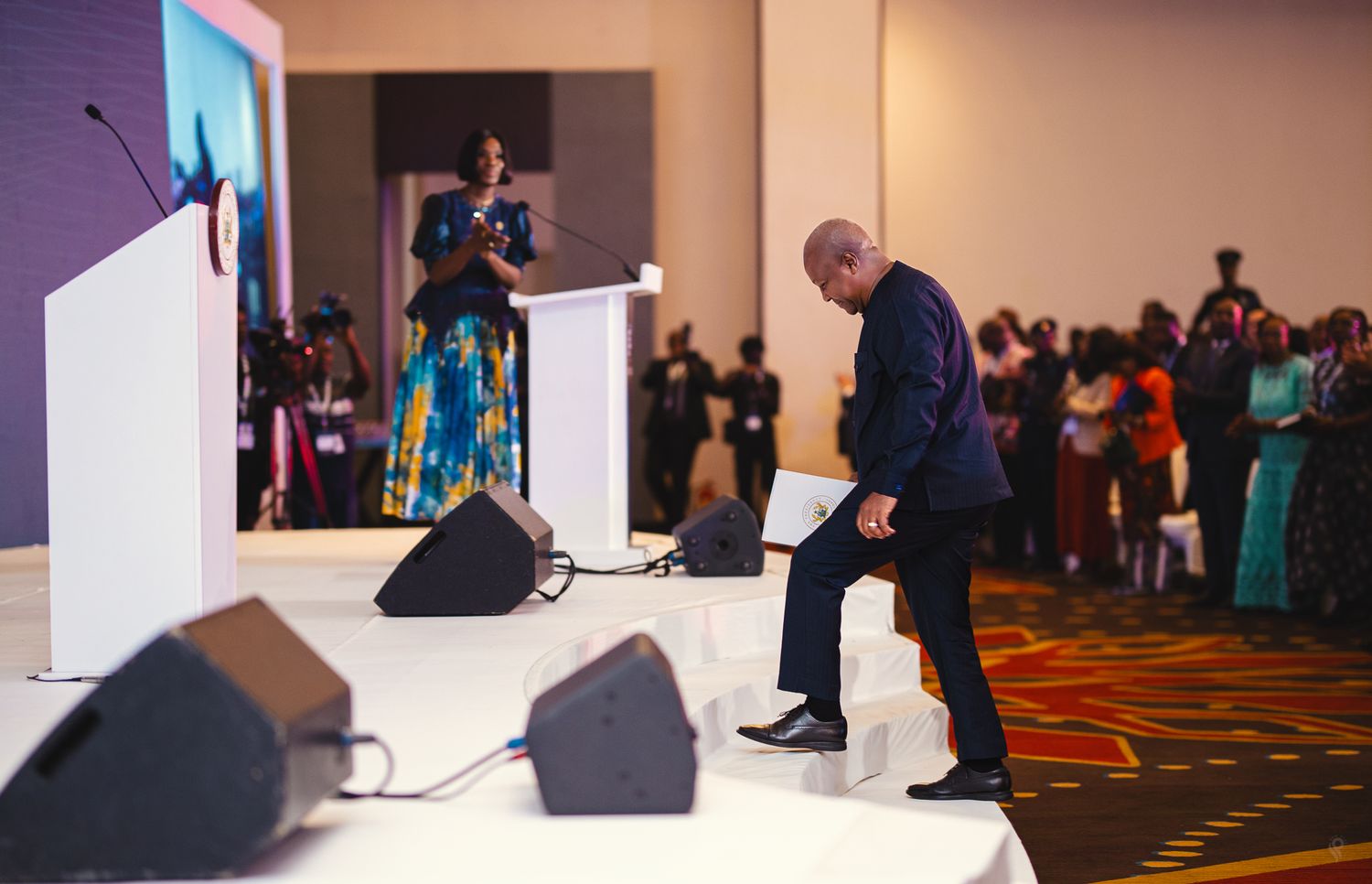 A man bows respectfully on stage at a formal Africa Trading Summit event before a large audience.