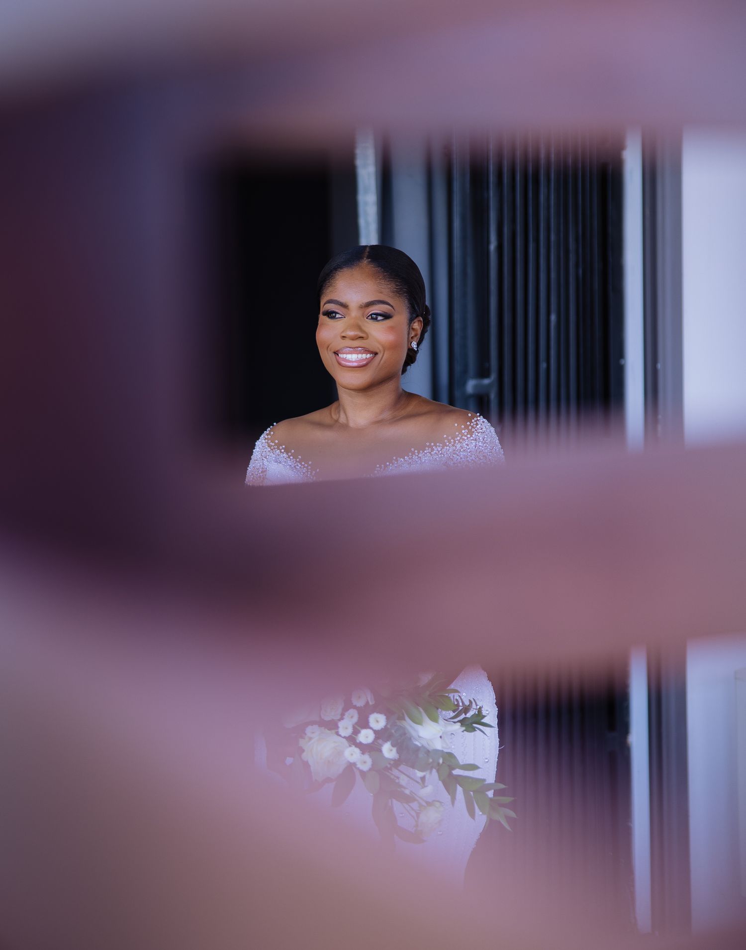Beautiful bride in white beaded gown smiles softly, photographed through a creative framed perspective.