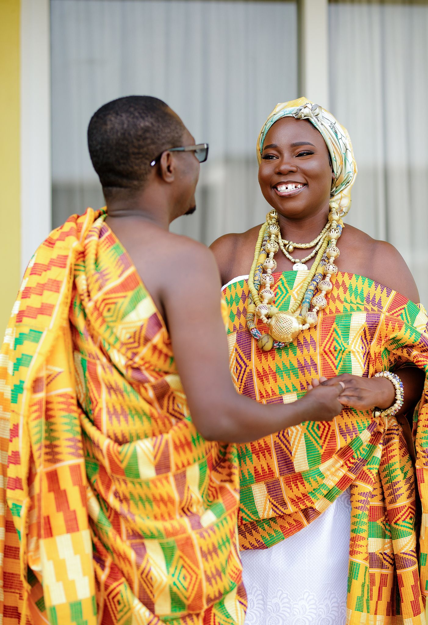 Couple in vibrant kente traditional attire share a joyful moment during a Ghanaian traditional wedding ceremony.
