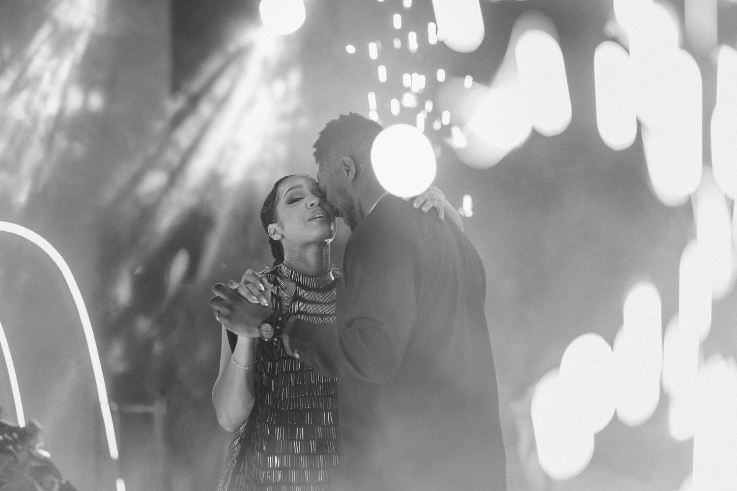 Black and white romantic couple sharing first dance under bokeh lights at wedding reception.