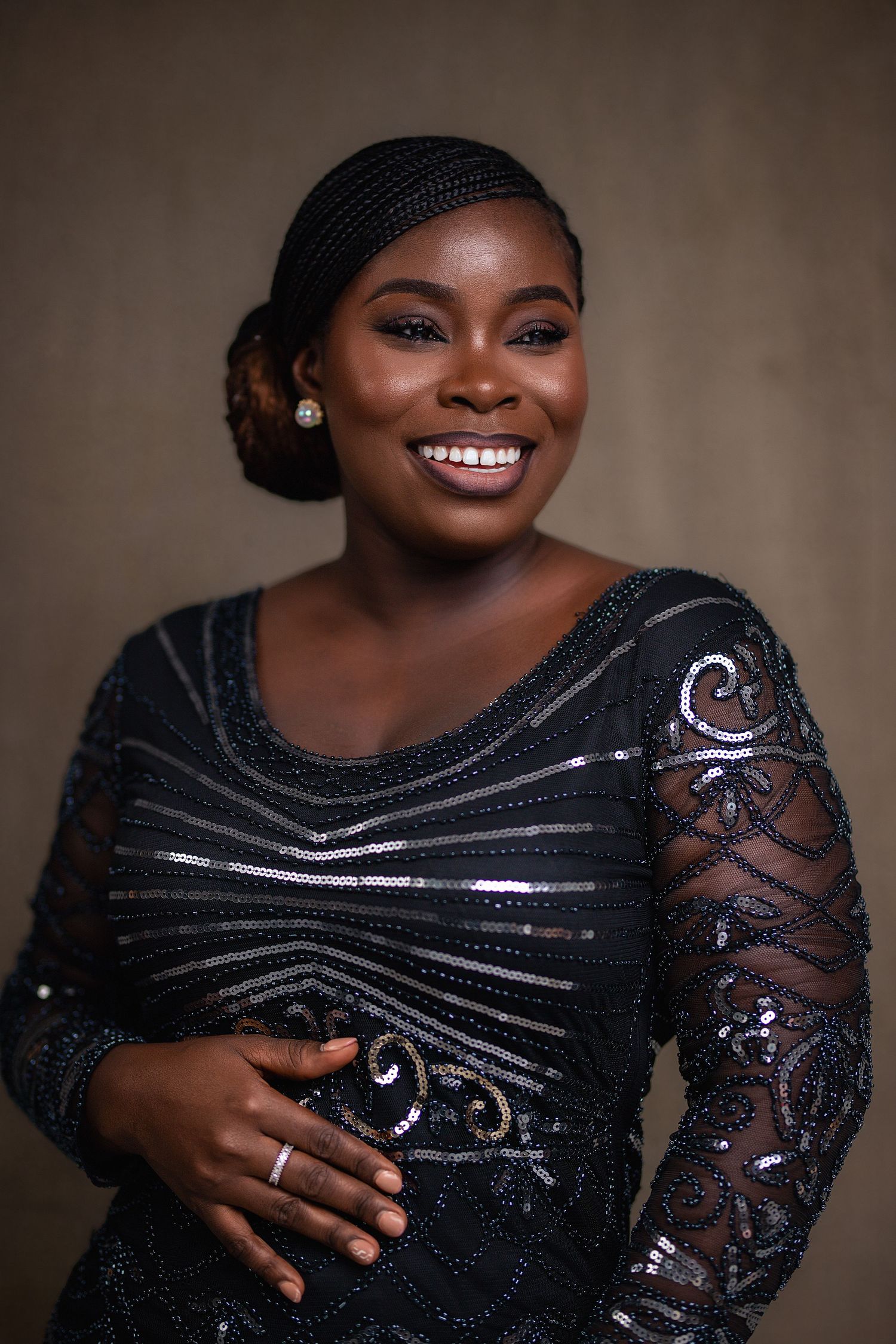 Smiling woman in black sequined lace dress in warm-toned professional studio portrait.