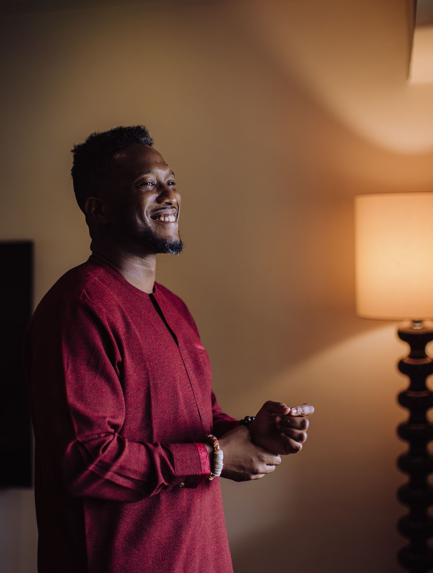 Joyful man in red traditional African attire laughing warmly in warmly lit elegant room.