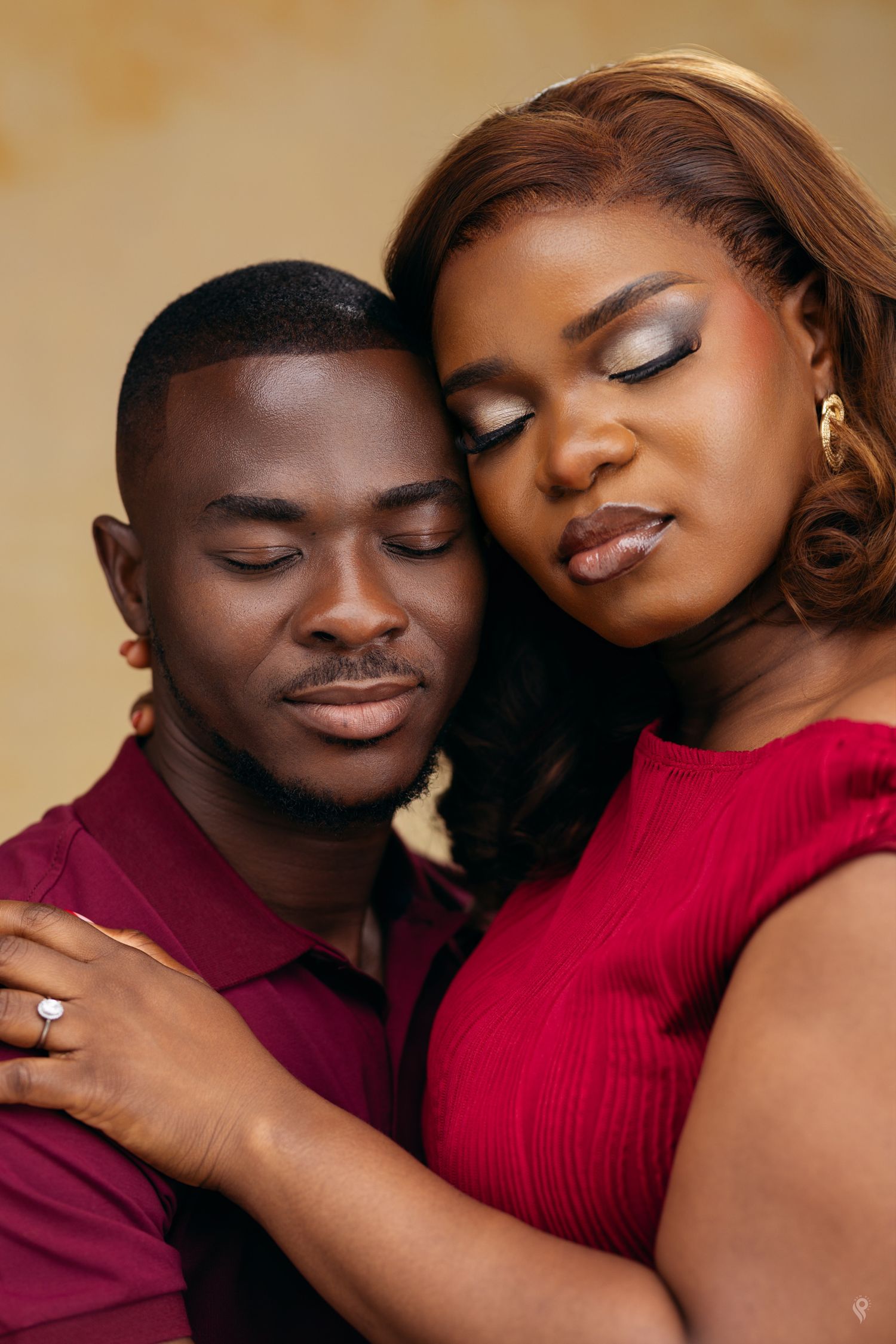 An intimate couple portrait with a man and woman in red and burgundy outfits with eyes closed.