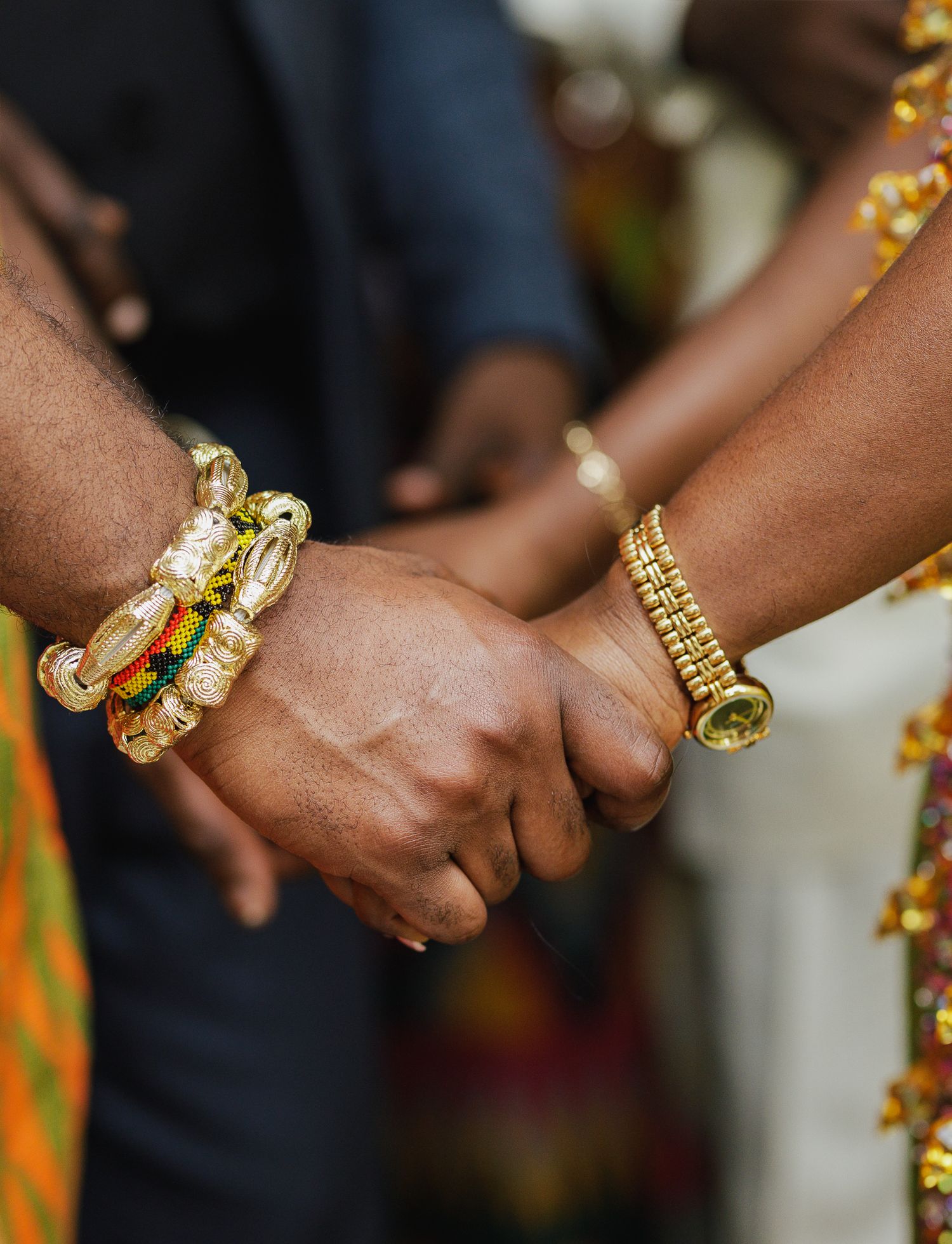 Couple holding hands adorned with gold bracelets at a traditional ceremony.