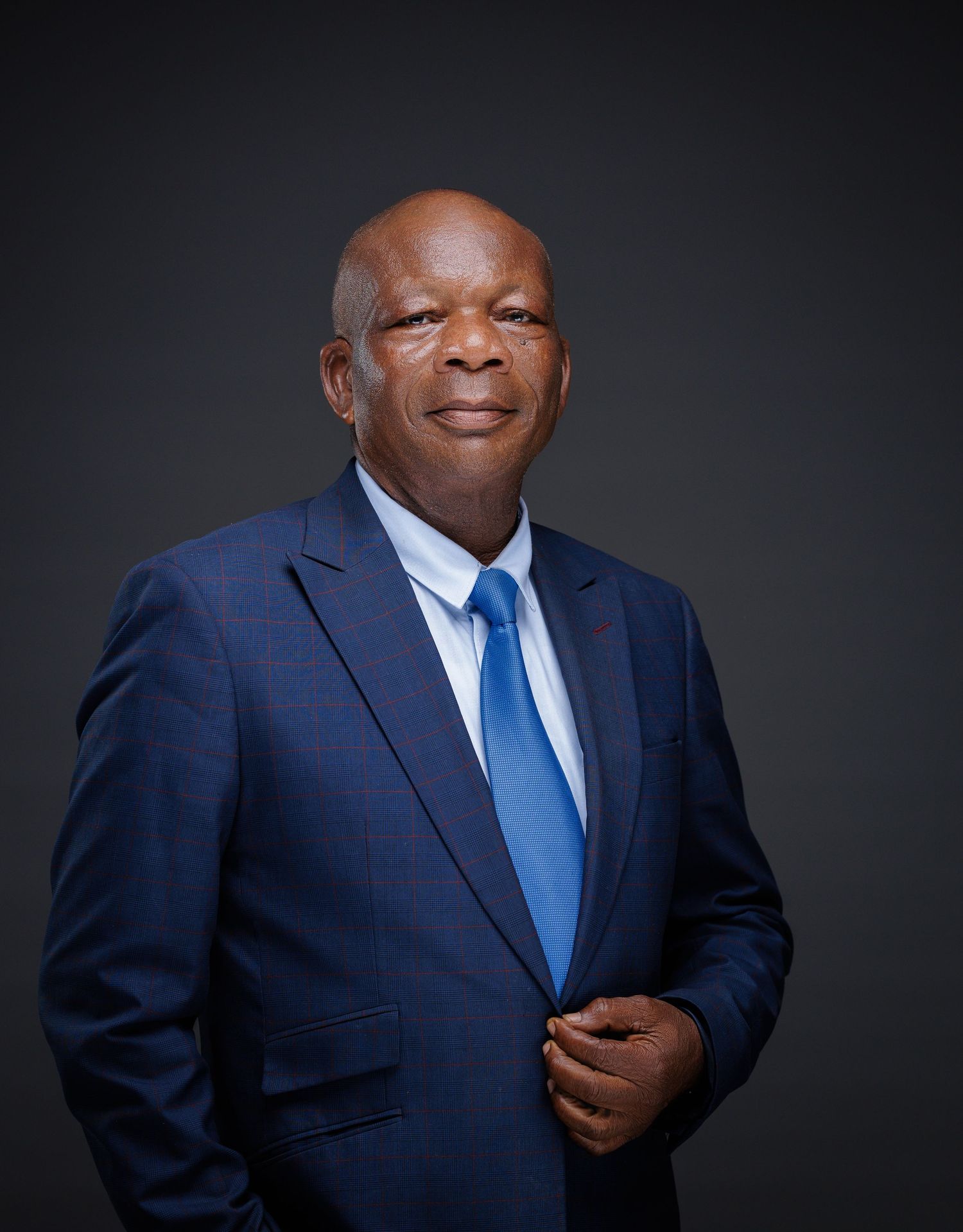 Mature man in blue suit adjusting jacket in formal professional studio portrait photography.
