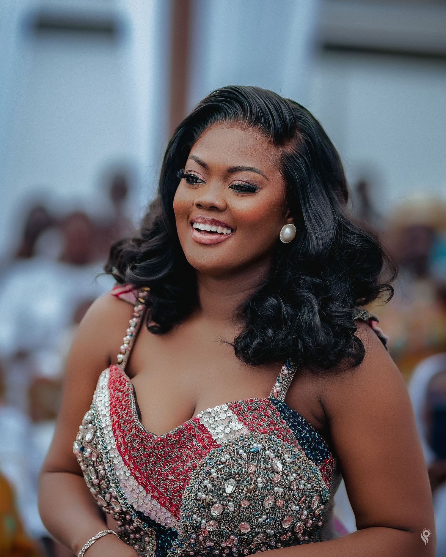 Elegant woman in beaded colorful strapless gown with pearl earrings smiling at an event.