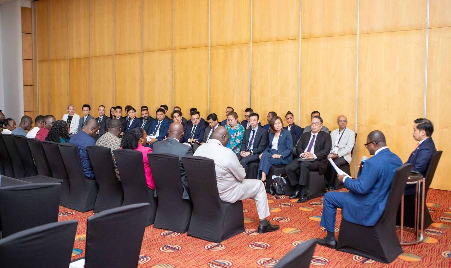 Business professionals attending a formal conference meeting seated in rows in a modern hall.