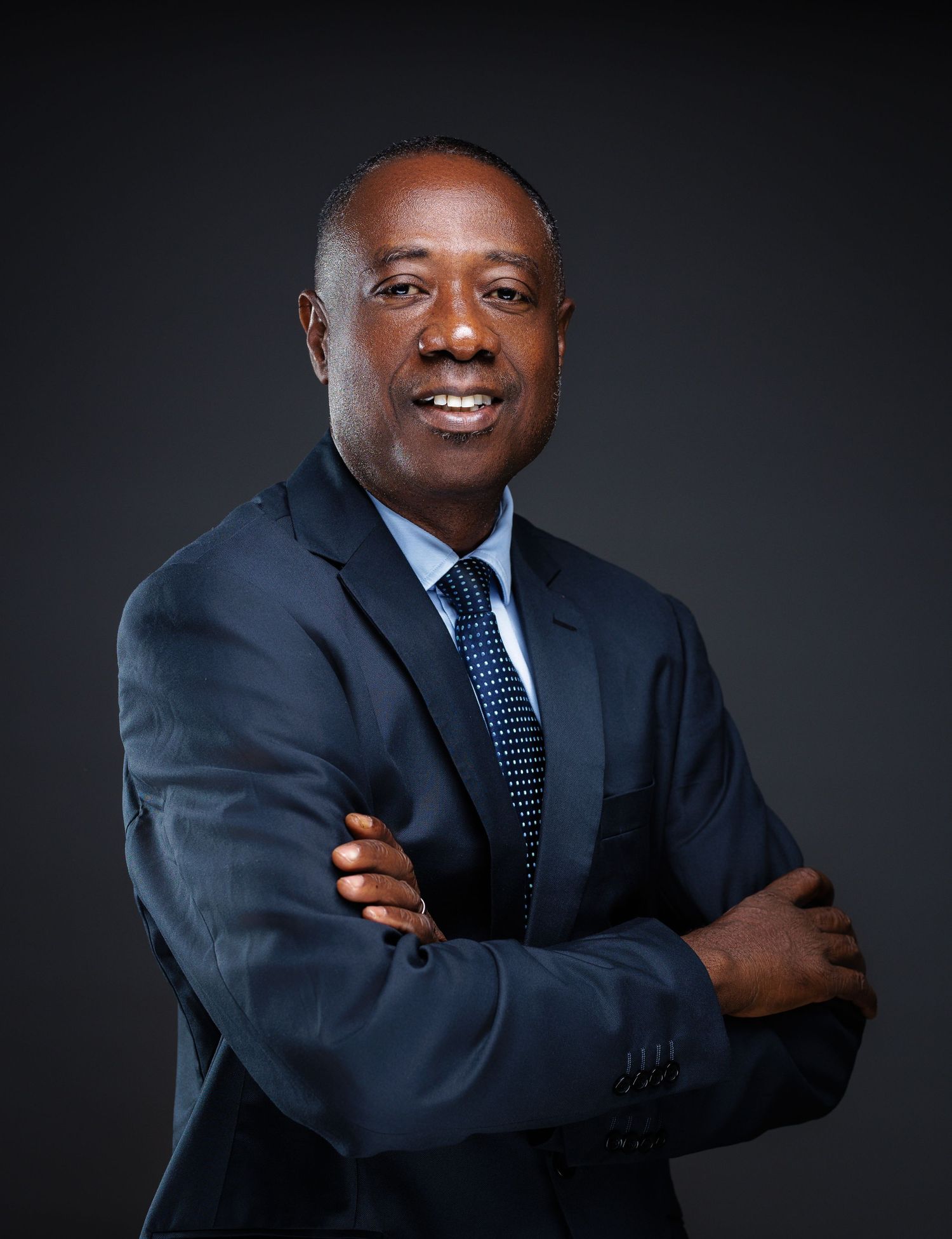Confident man in navy suit with arms crossed smiling in professional business portrait.
