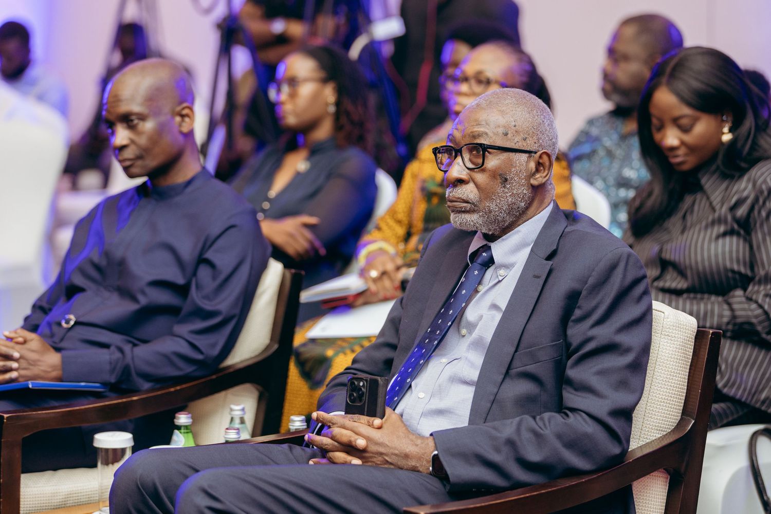 Elderly gentleman and younger man seated attentively at professional business conference.