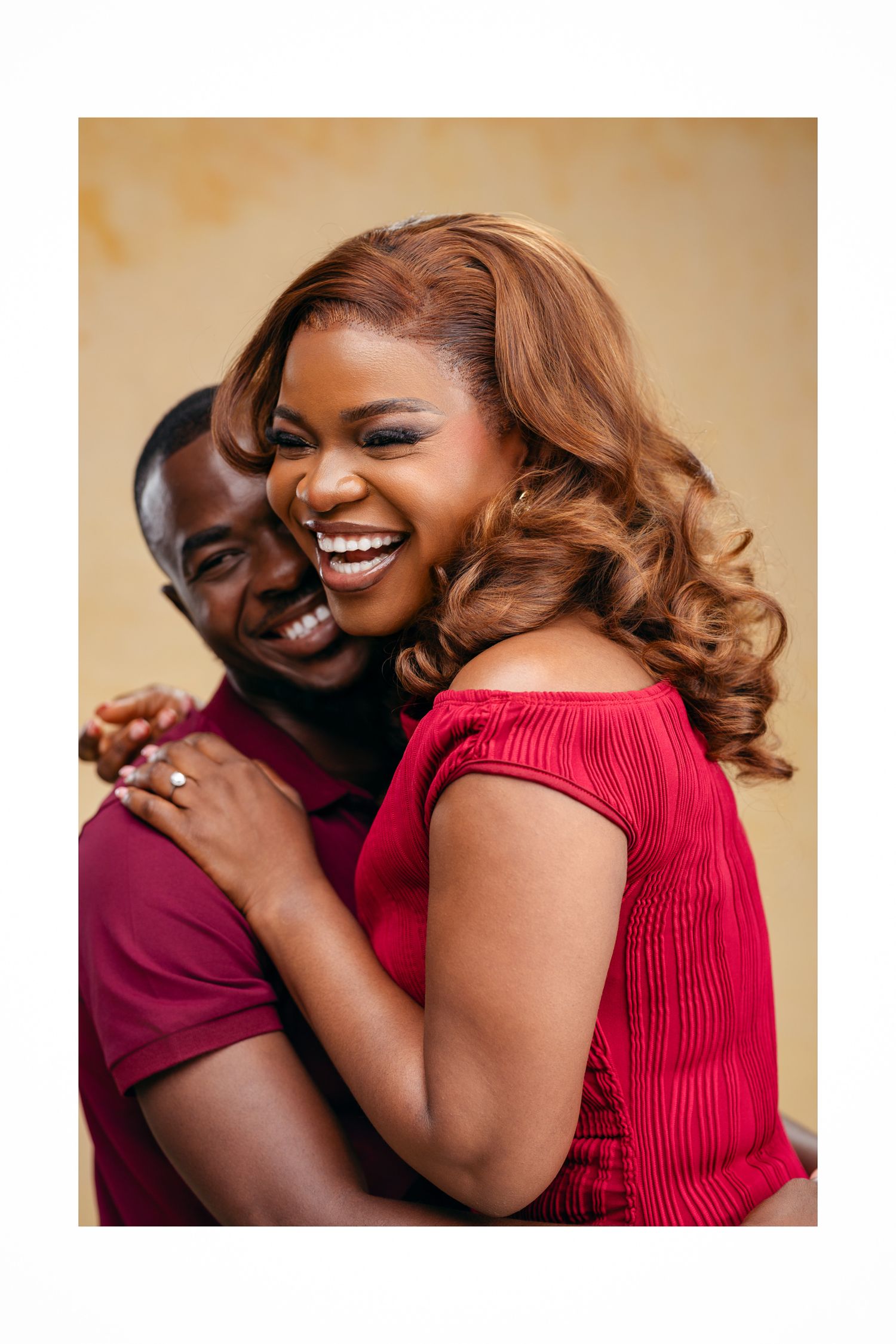 Joyful couple in red outfits laughing and embracing during a romantic photo session.