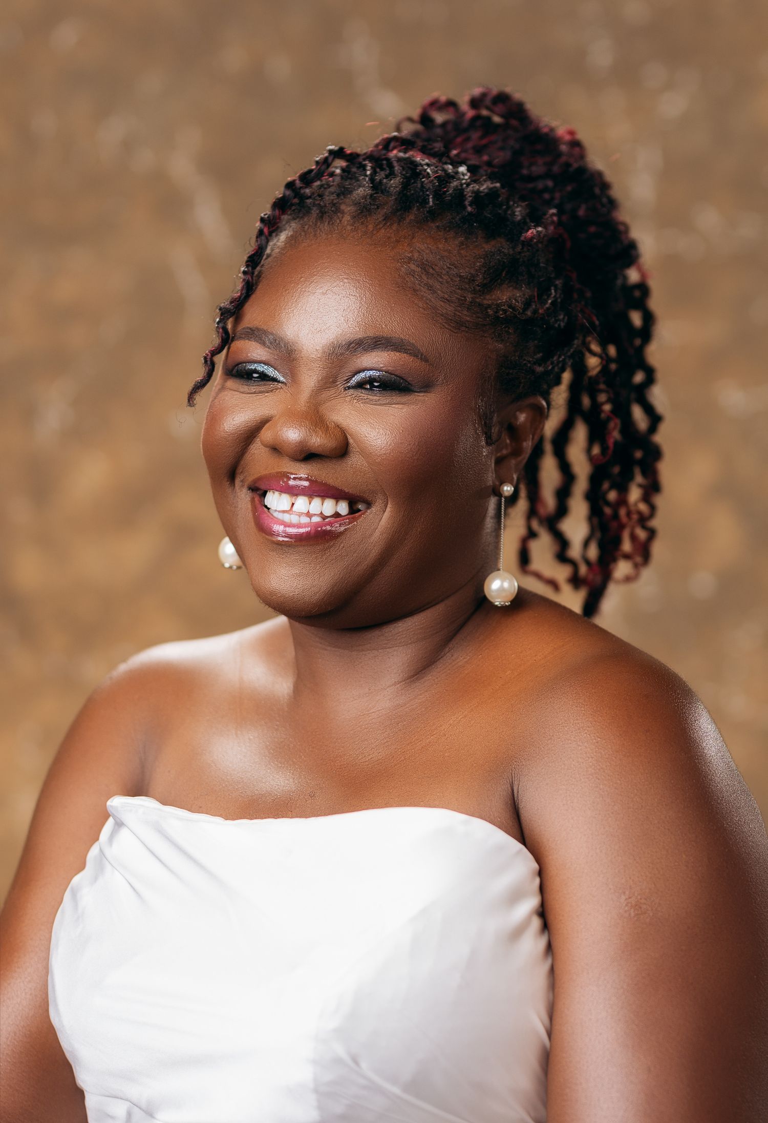 Smiling woman with colorful locs in white strapless dress poses for professional portrait.