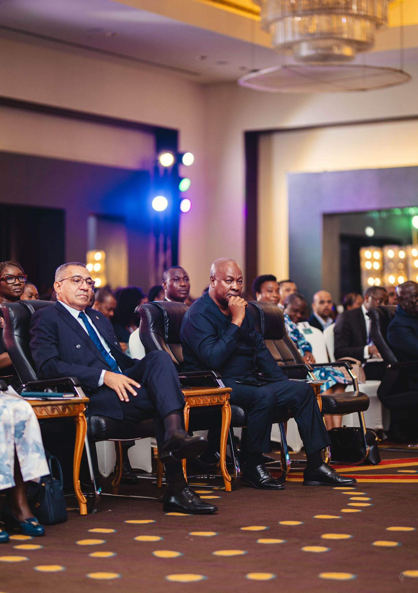 Distinguished guests seated in golden chairs attentively watching a presentation at a gala event.