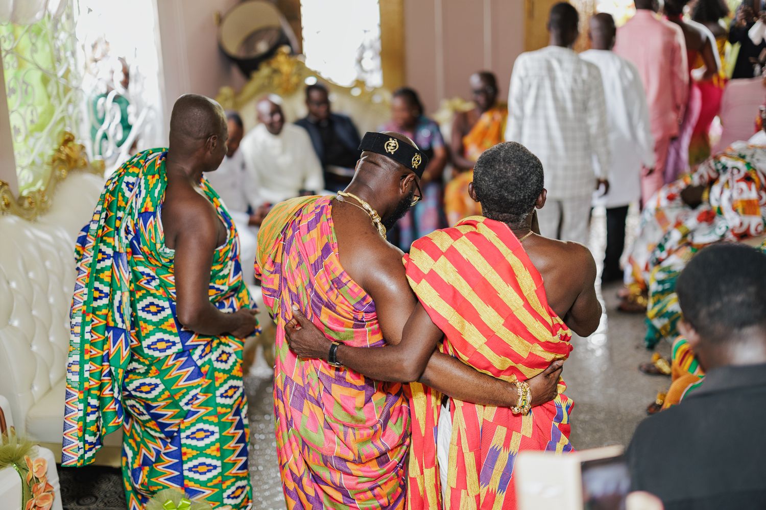Guests in traditional Kente cloth embrace during an African wedding ceremony.