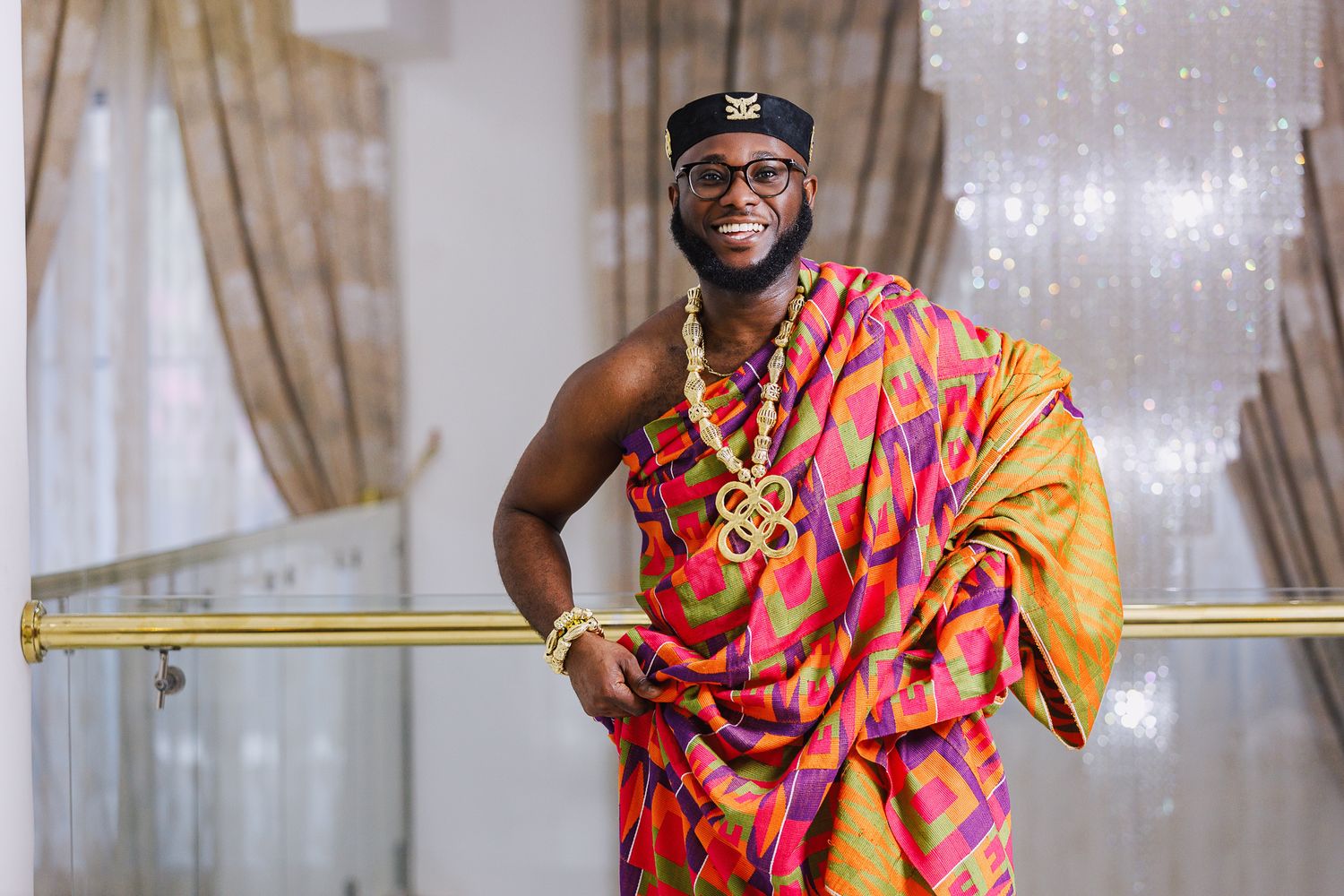 Man in colorful Kente cloth traditional Ghanaian attire smiling confidently.
