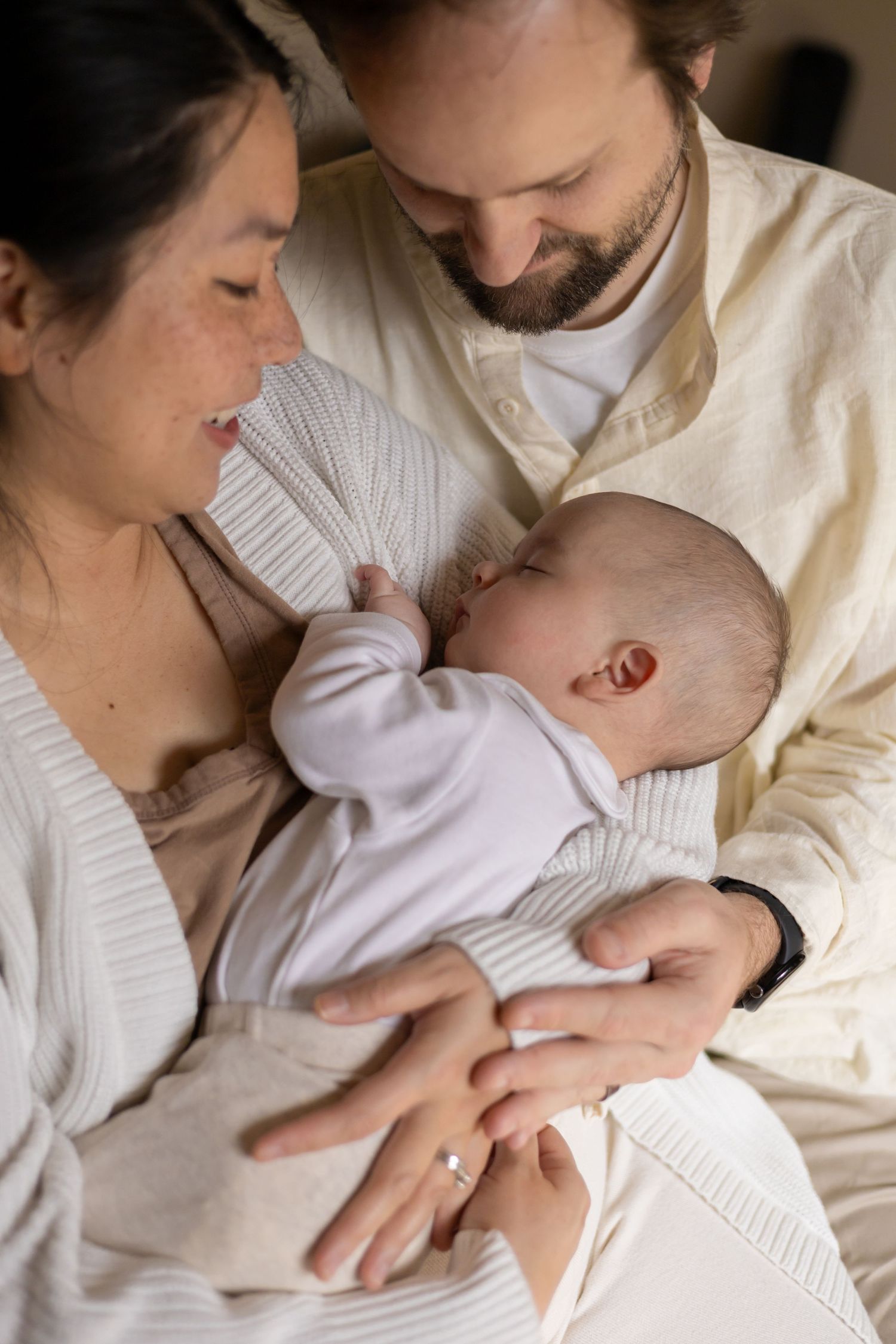 Couple cuddling their newborn baby in their bedroom during an in home newborn lifestyle session