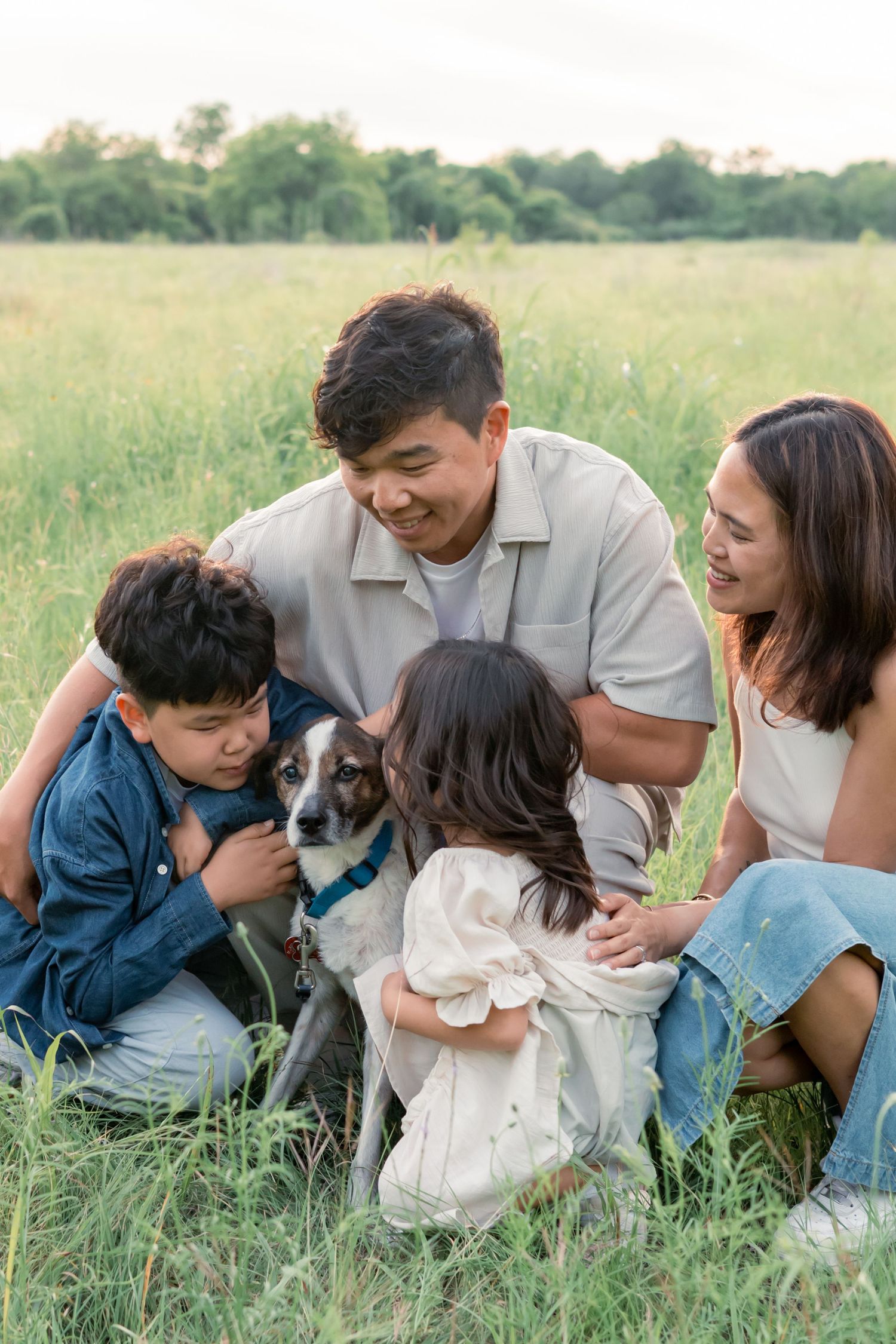 Family laughing together embracing their dog in a grassy field