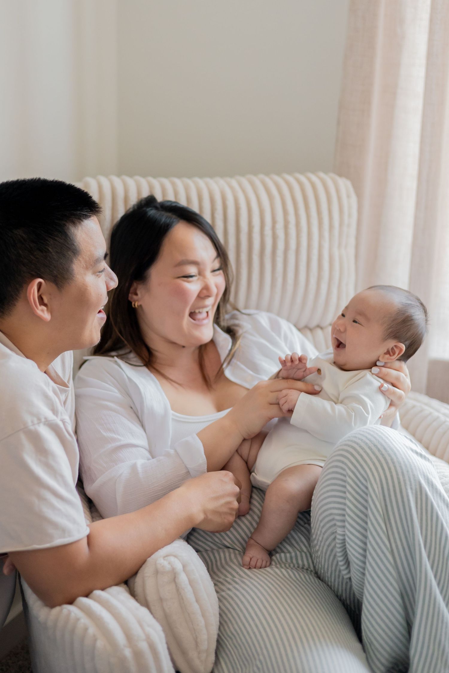Parents laughing and playing with their baby during a natural light newborn lifestyle session in their nursery