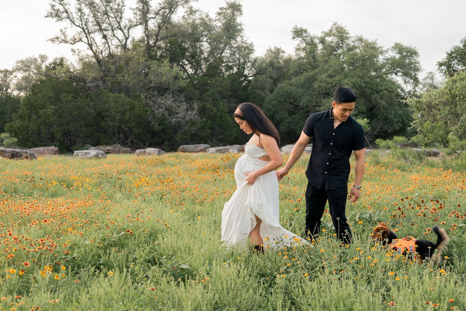 Pregnant Couple expecting their first child walking in a grassy field of wildflowers together during a sunset maternity session