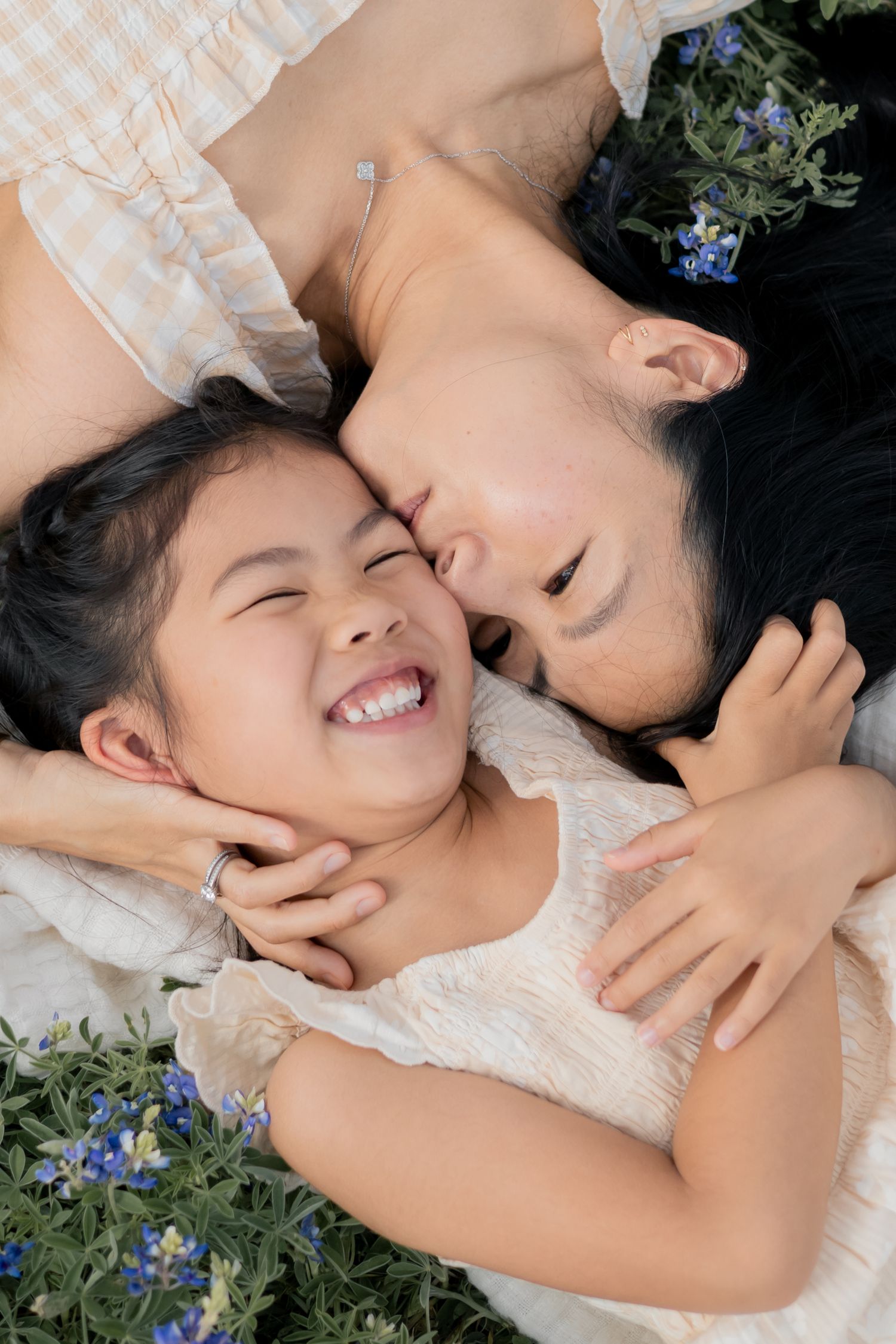 Mother kissing her daughter's cheek while laying in a grass of blue bonnets during a family lifestyle session