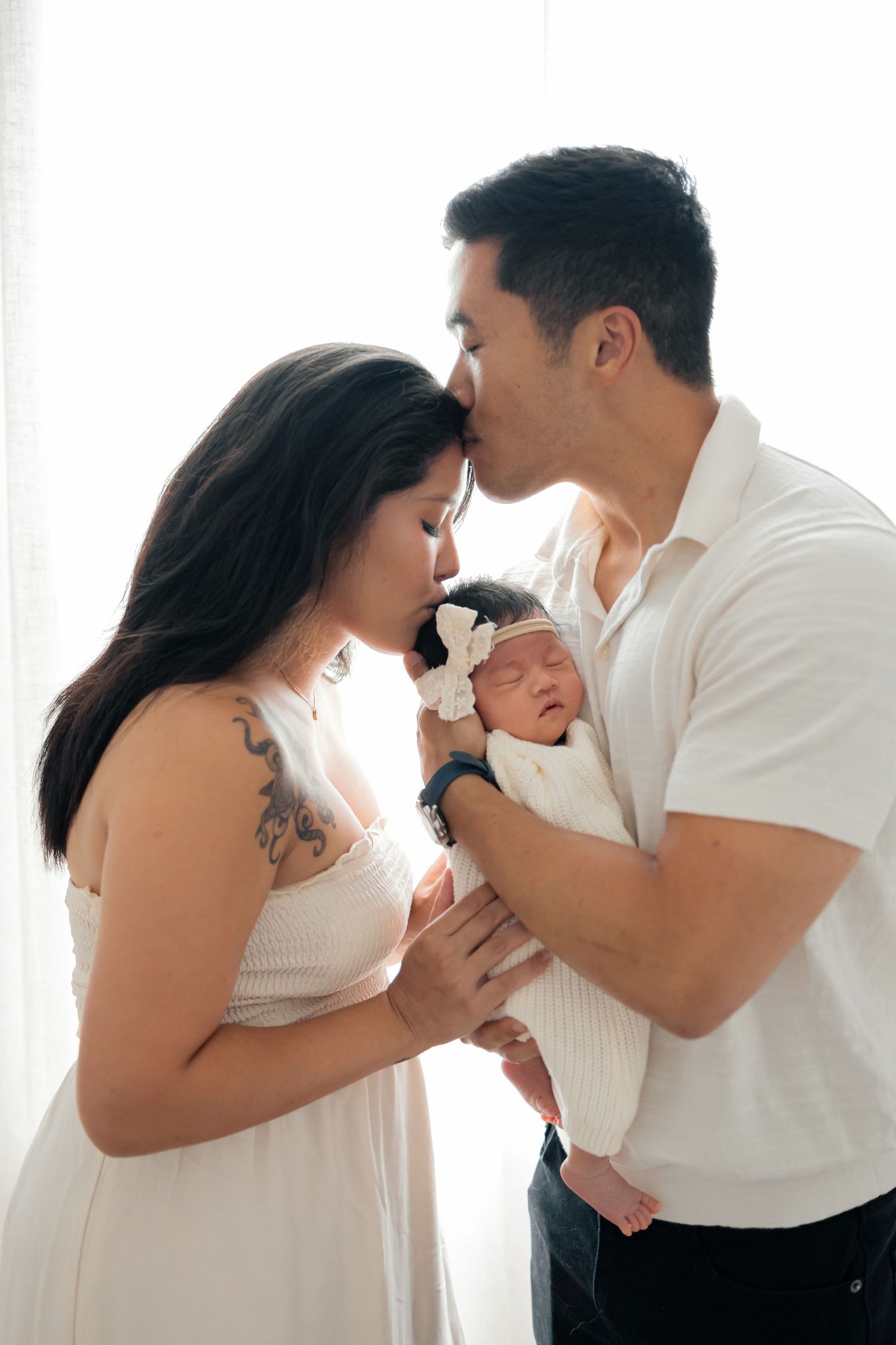 Parents kissing and cuddling newborn baby during a natural light lifestyle newborn session