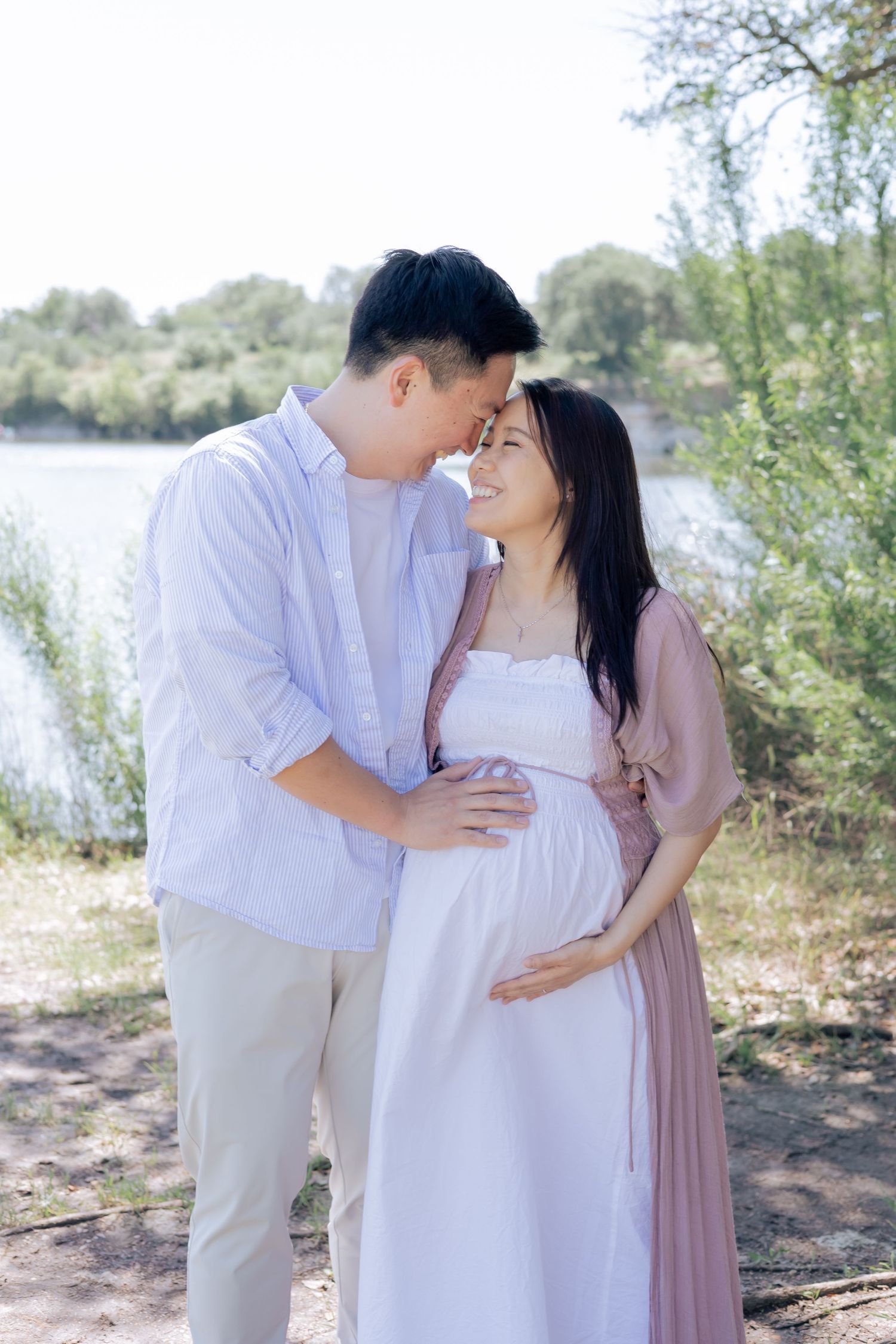 Couple embracing one another outside near a lake during a lifestyle family maternity session