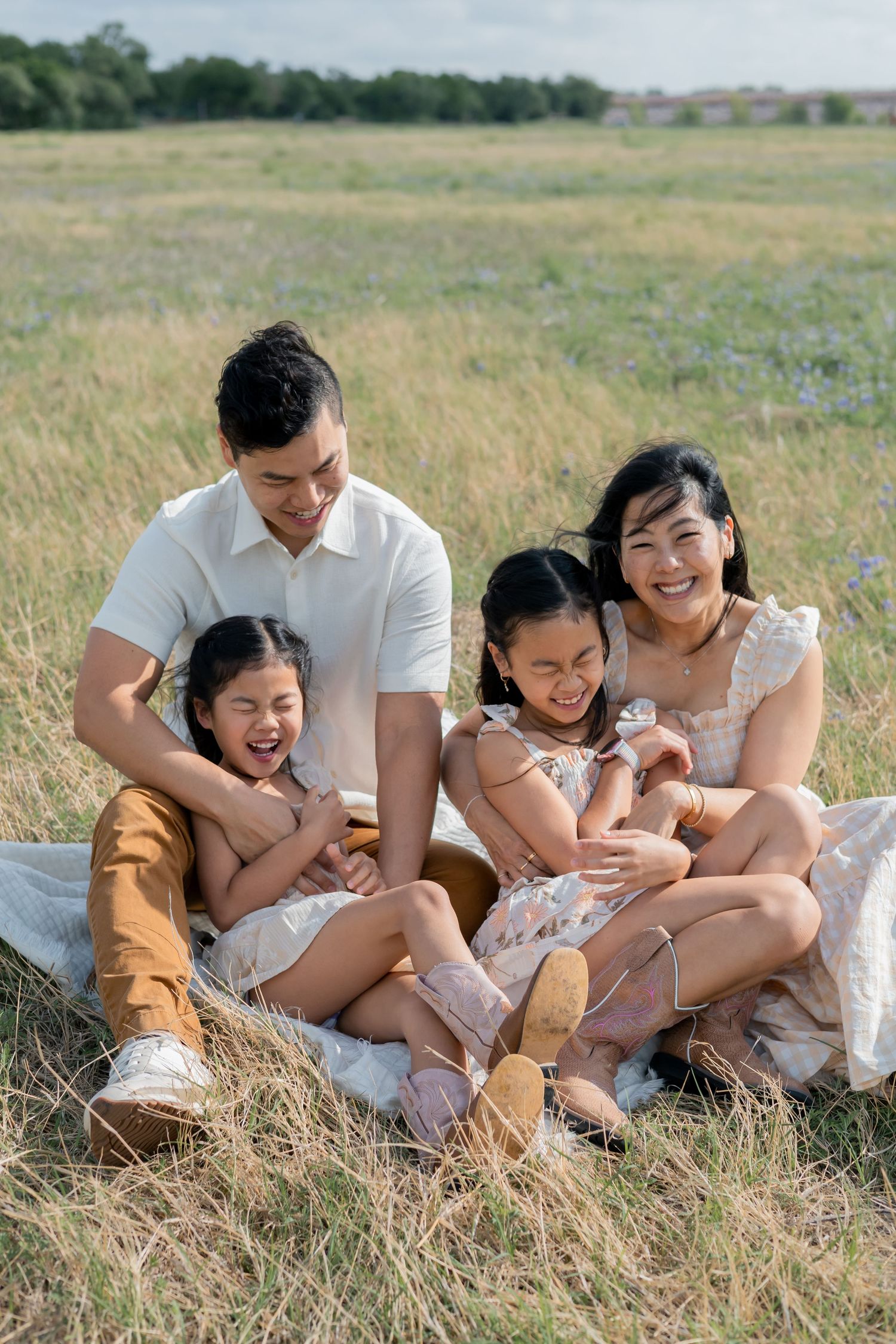 Family sitting and laughing together in a grassy field during a lifestyle family session