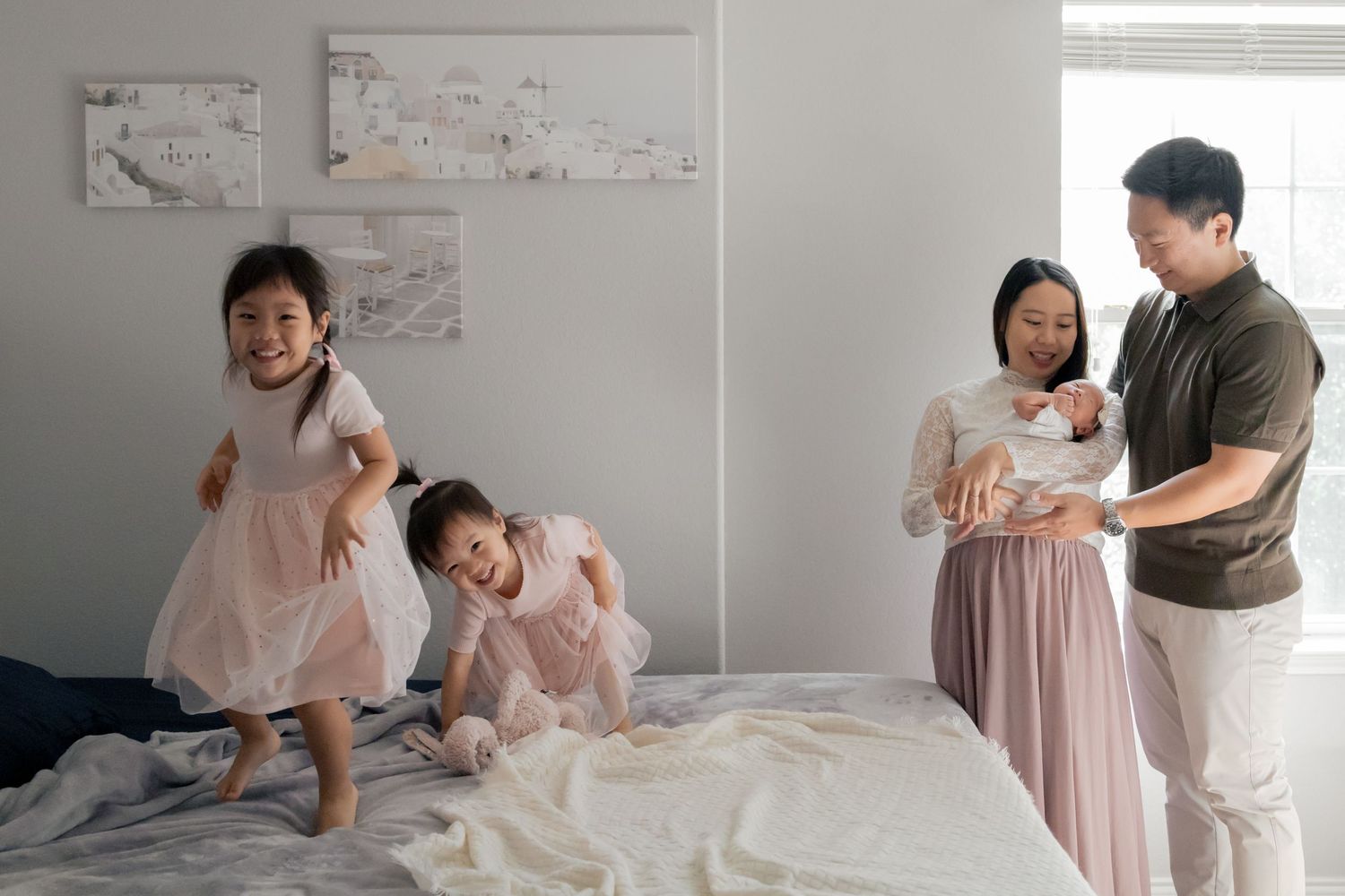 Siblings jumping on bed while parents hold newborn baby during a natural light lifestyle newborn session